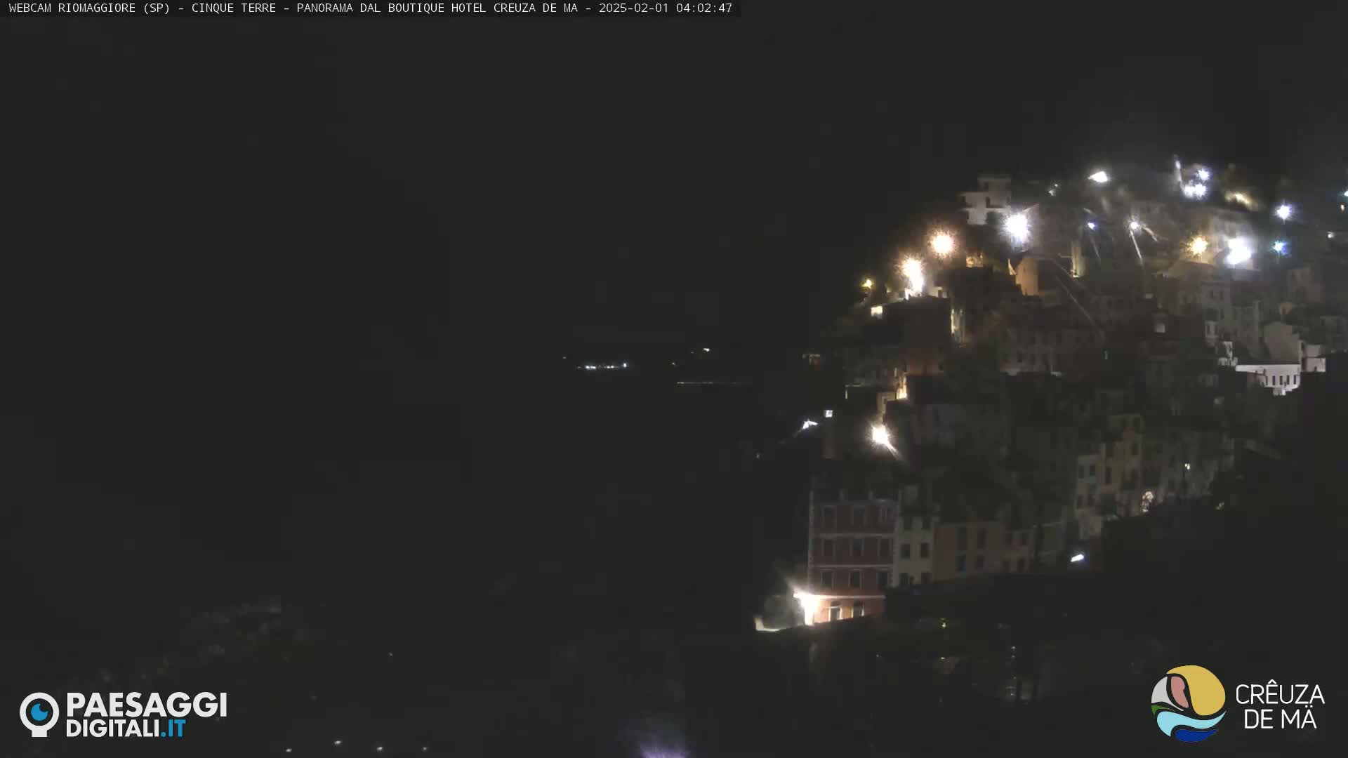 A nighttime view of a hillside village with fireworks illuminating buildings and the dark surrounding water.