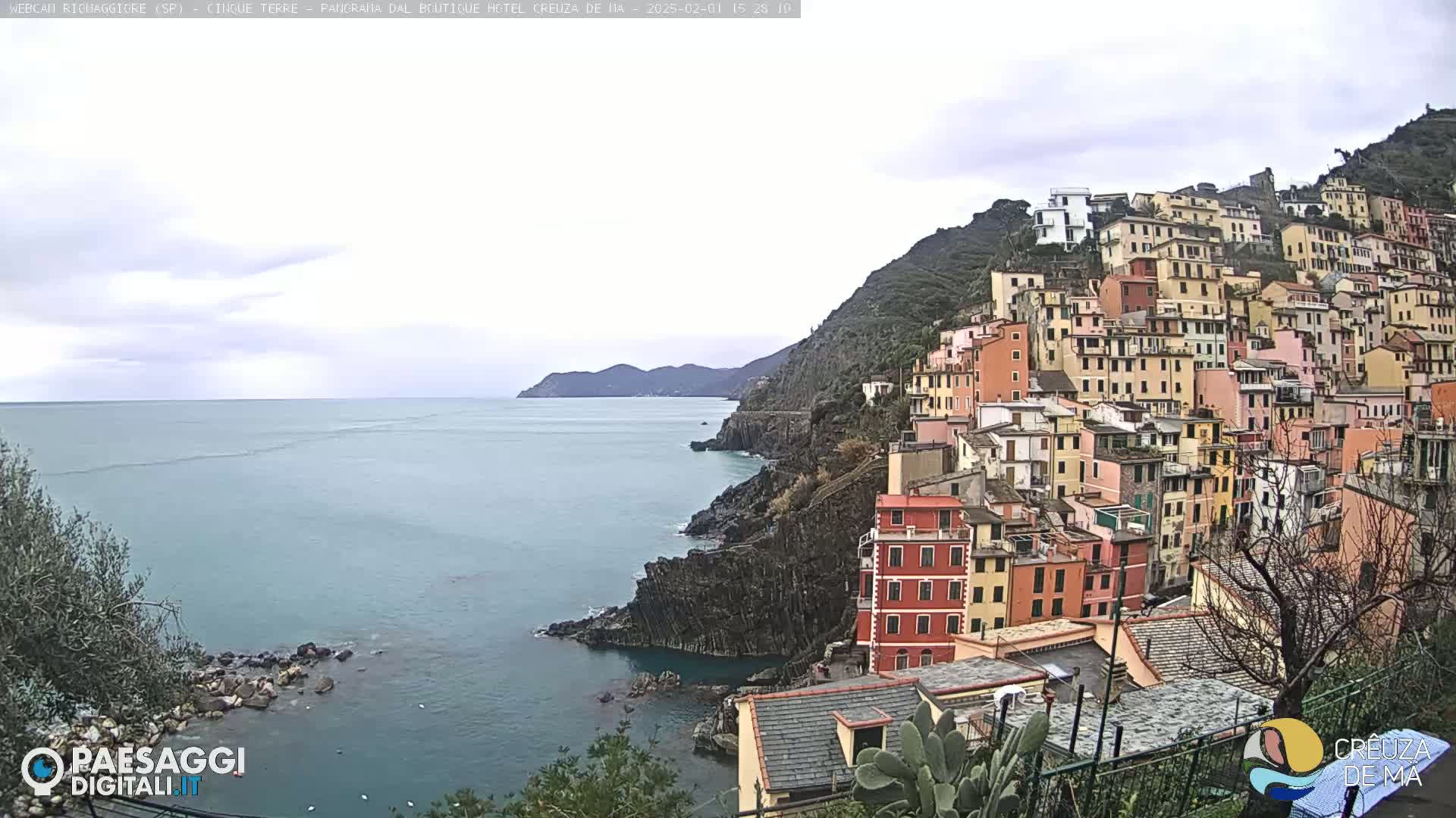 A coastal village with colorful buildings stacked on a hillside overlooking a calm sea under a cloudy sky.