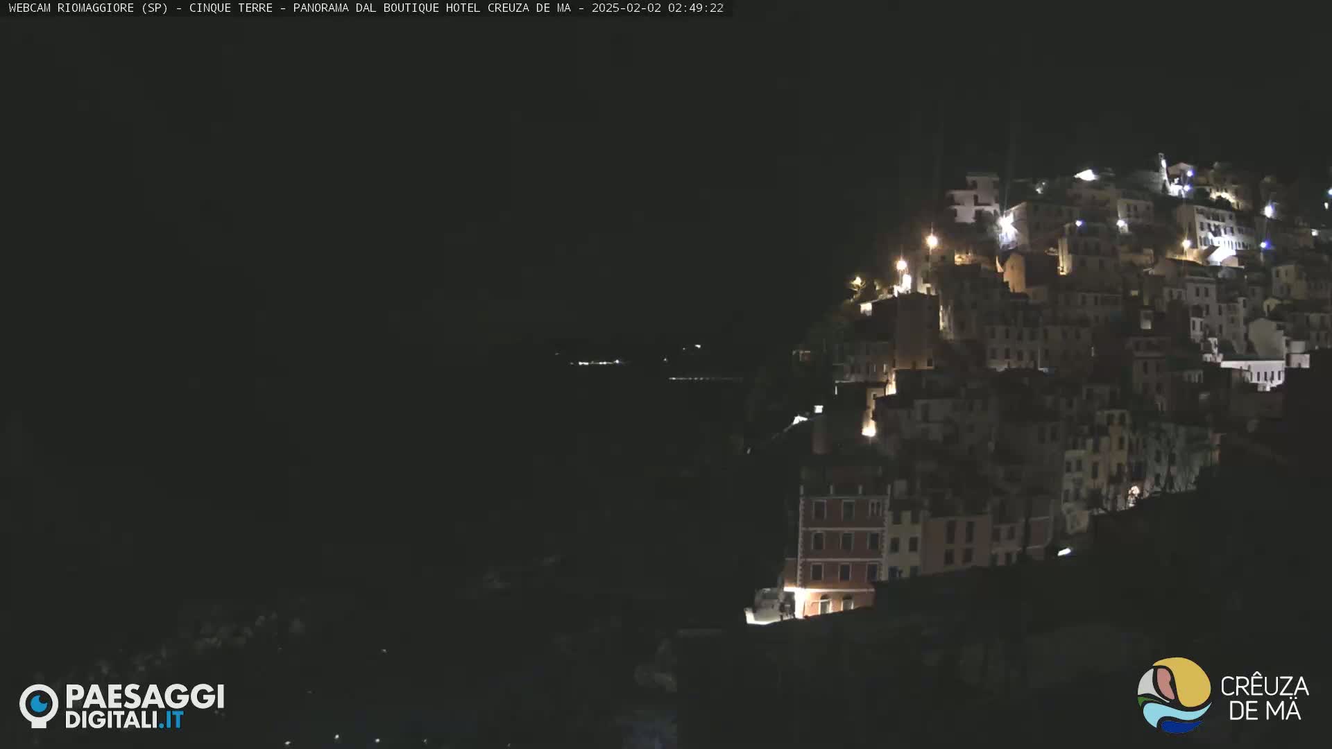 A hillside village is illuminated at night, overlooking a dark body of water.