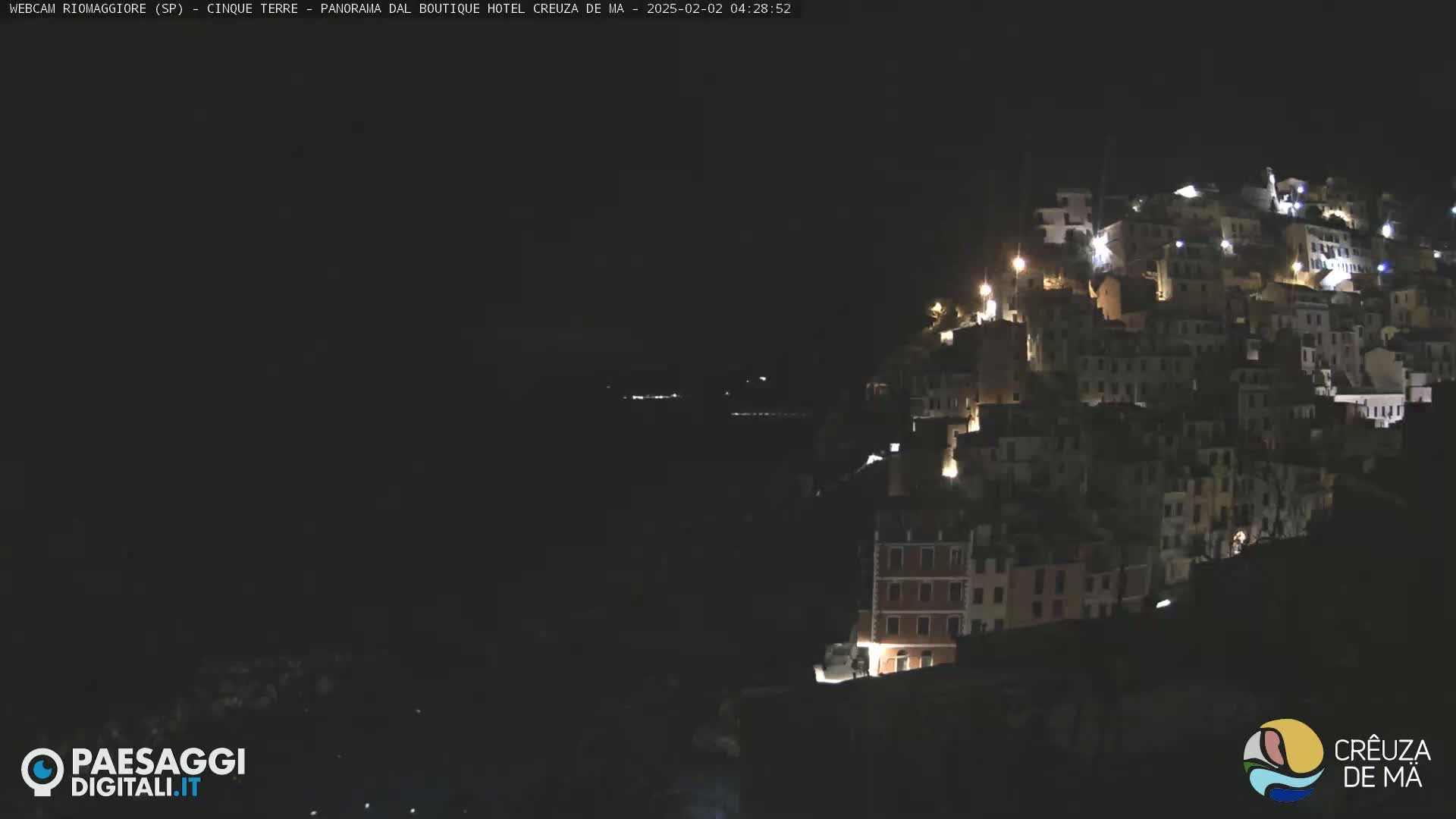 A hillside town is illuminated at night, overlooking a dark body of water.