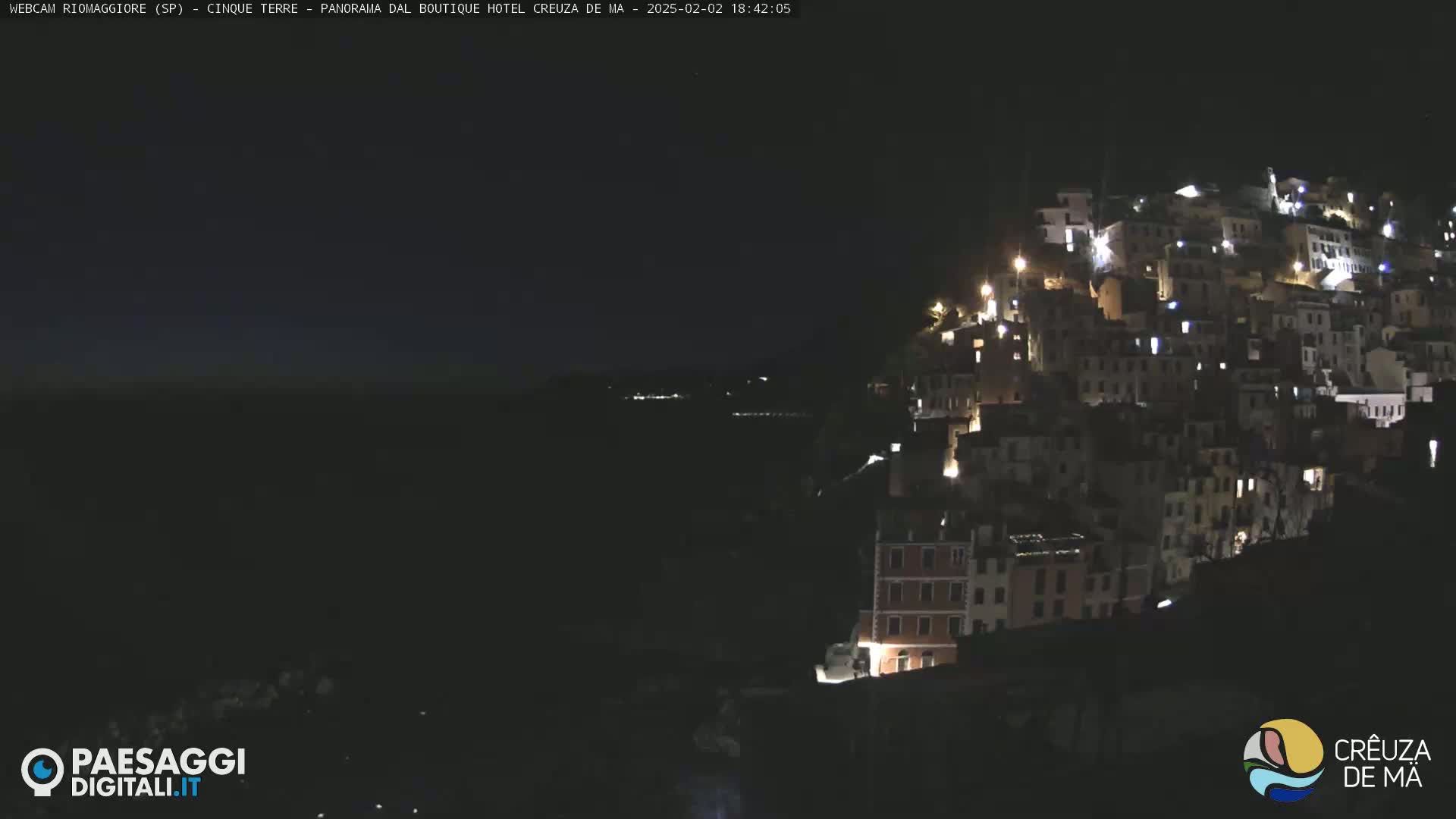 A nighttime, long shot of a hillside town illuminated by lights against a dark sky.