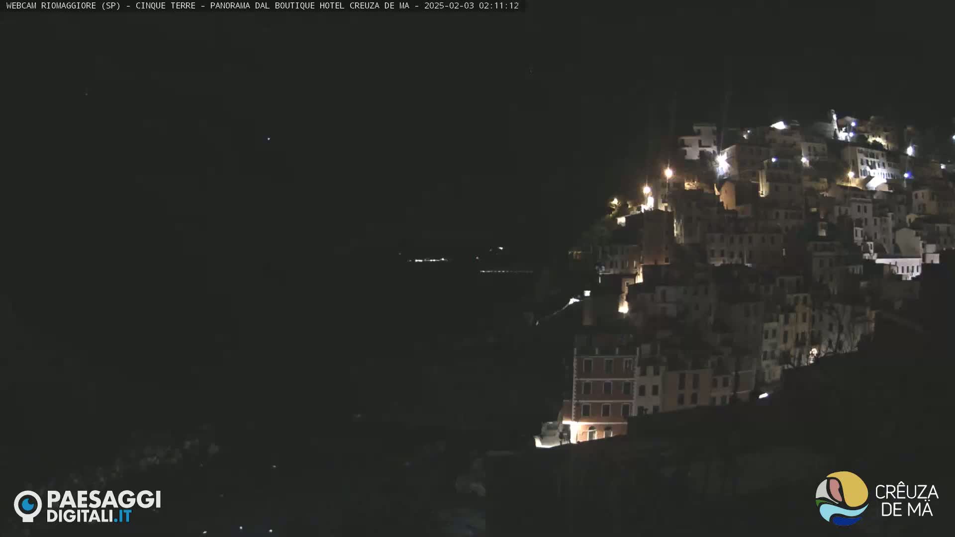 A hillside town is illuminated at night under a dark, clear sky.