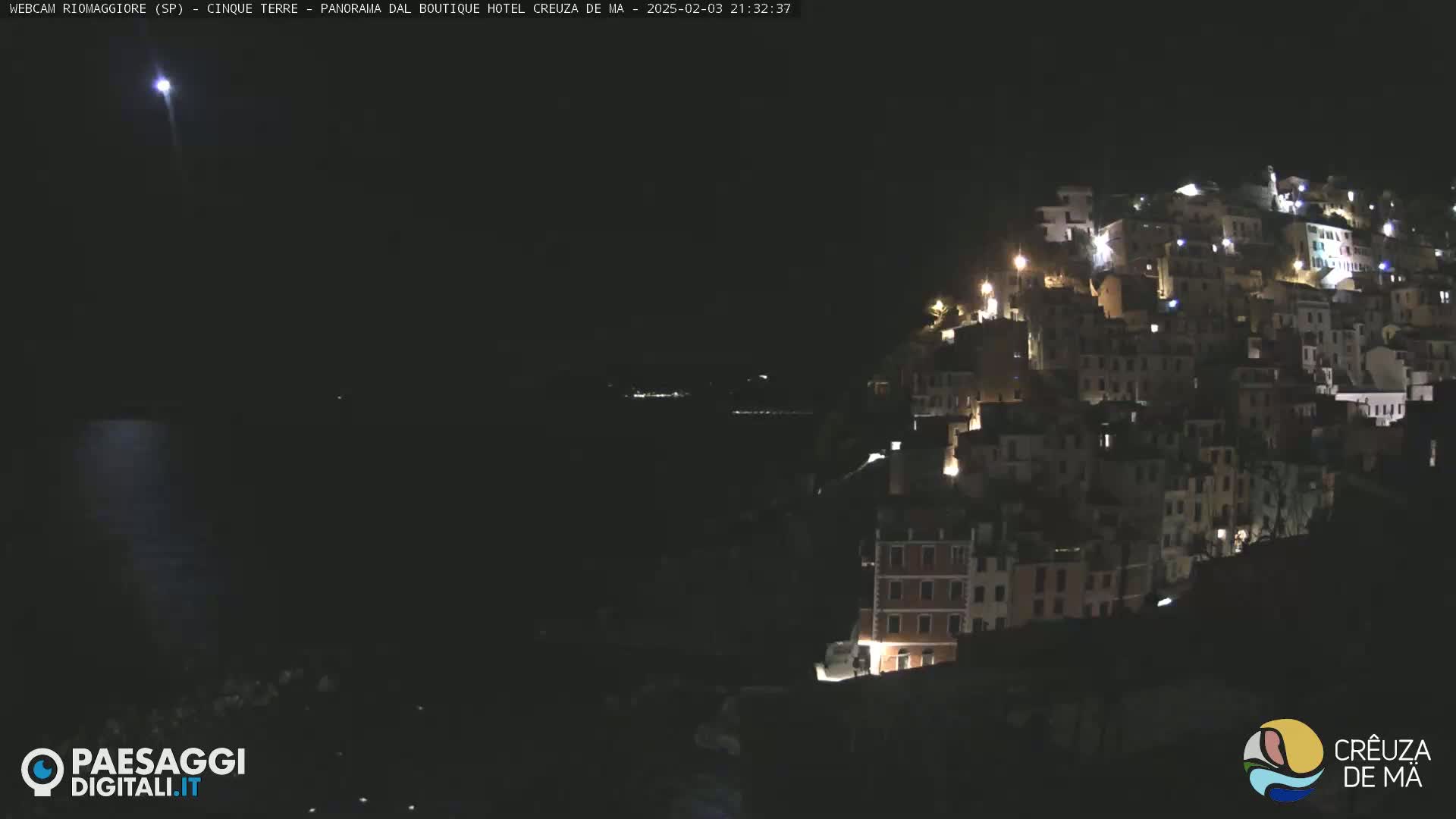 A nighttime view of a hillside town with many lit windows, under a dark, clear sky.