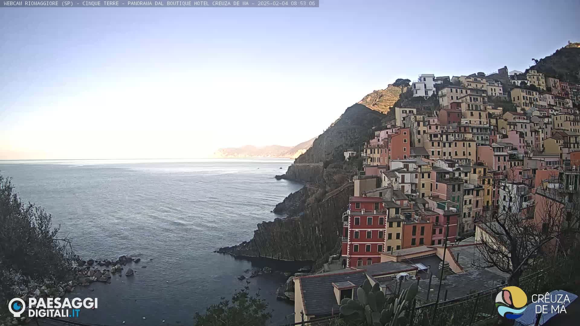 A coastal town with colorful buildings clinging to a steep cliffside overlooks a calm sea under a clear sky.