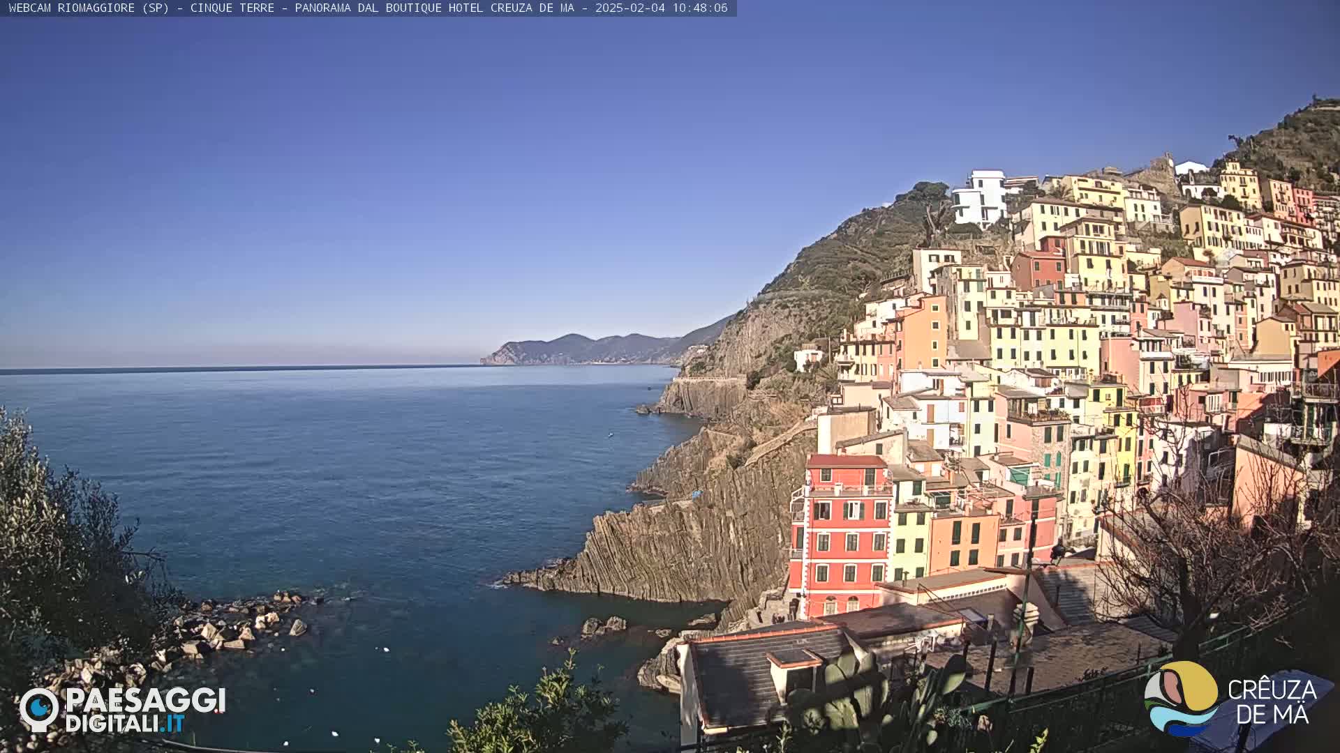 A colorful hillside village overlooks a calm blue sea under a clear sky.