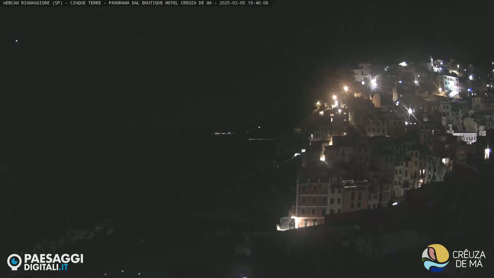 A nighttime view of a hillside village illuminated by lights, overlooking a dark body of water.