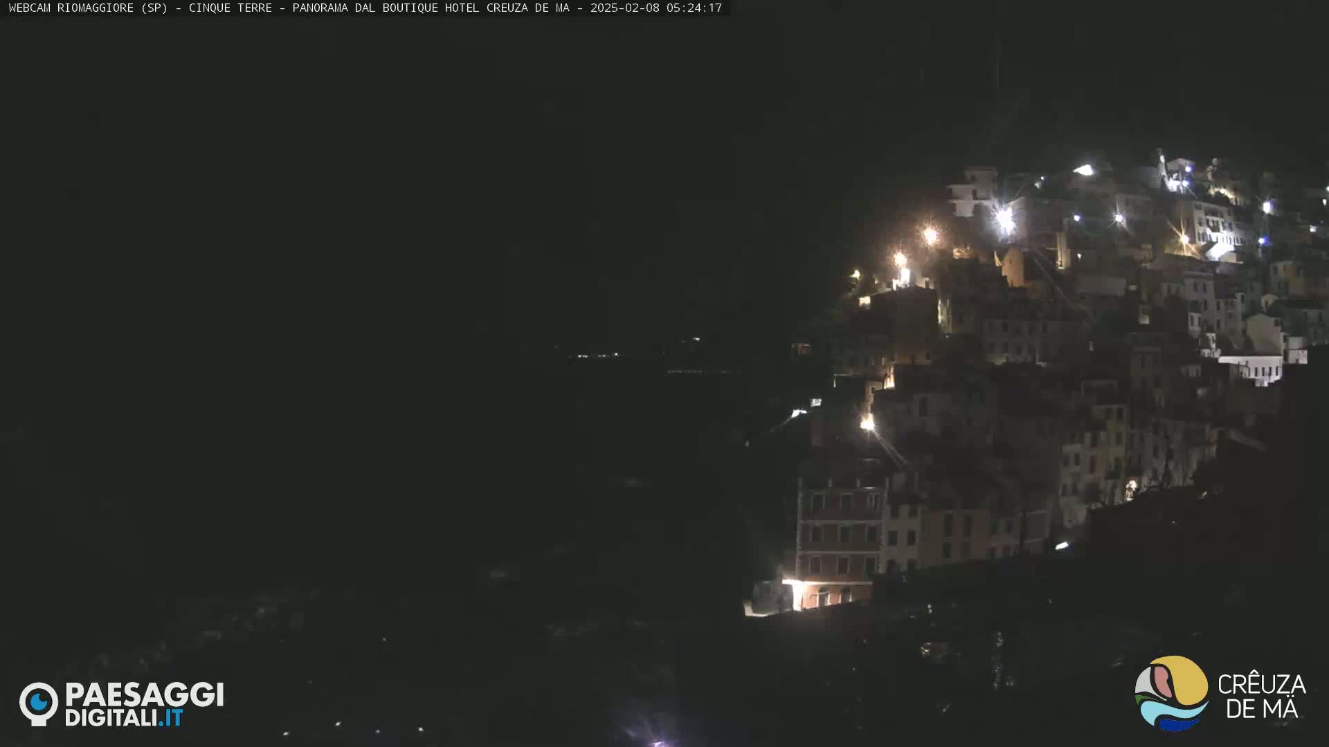 A nighttime, long shot of a hillside town with illuminated buildings.