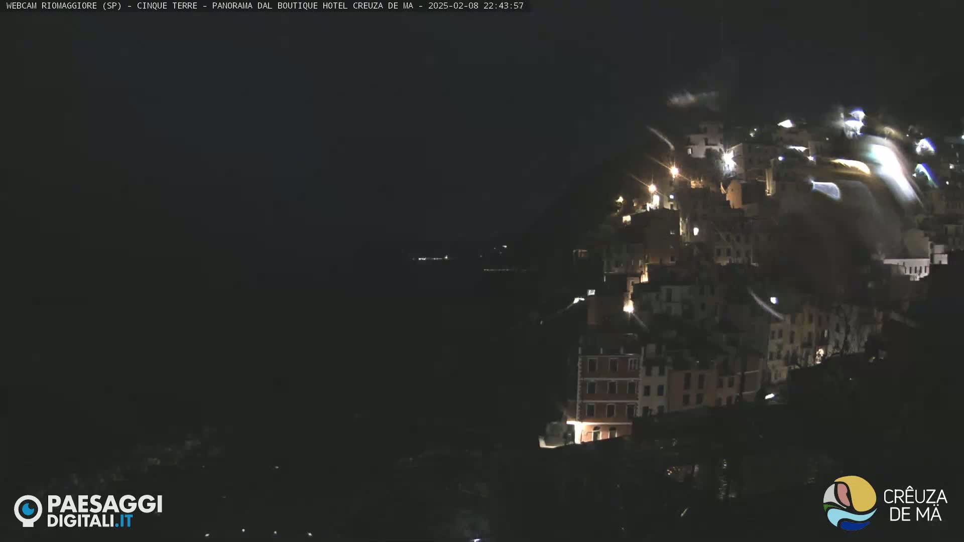 A nighttime view of a hillside town illuminated by scattered lights, with dark water visible below.