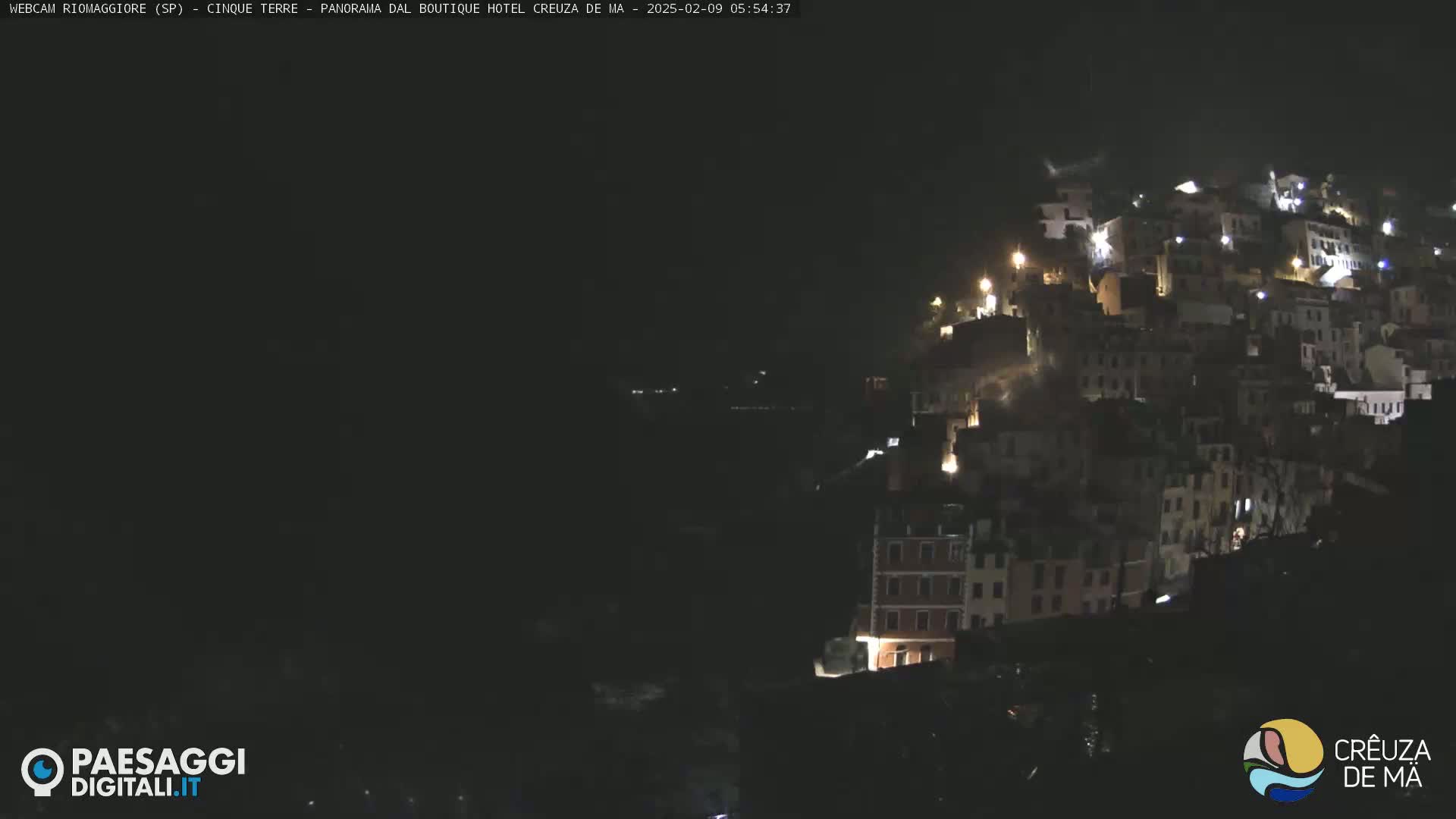 A nighttime view of a hilltop village with dimly lit buildings under a dark sky.
