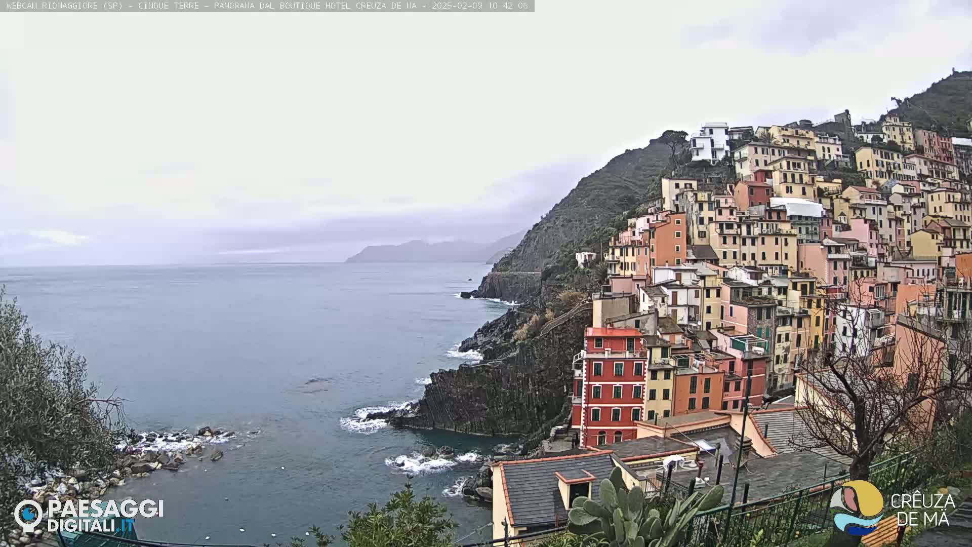 A colorful hillside town overlooks a gray, overcast ocean.