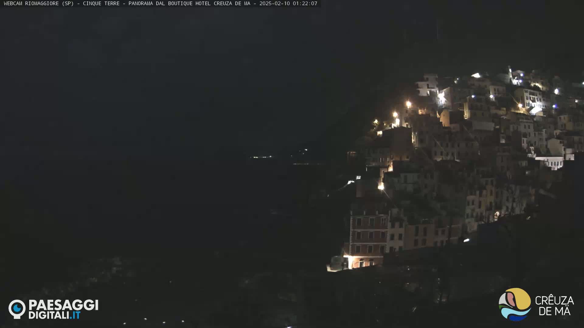 A nighttime view of a hillside town with illuminated buildings overlooking a dark body of water.