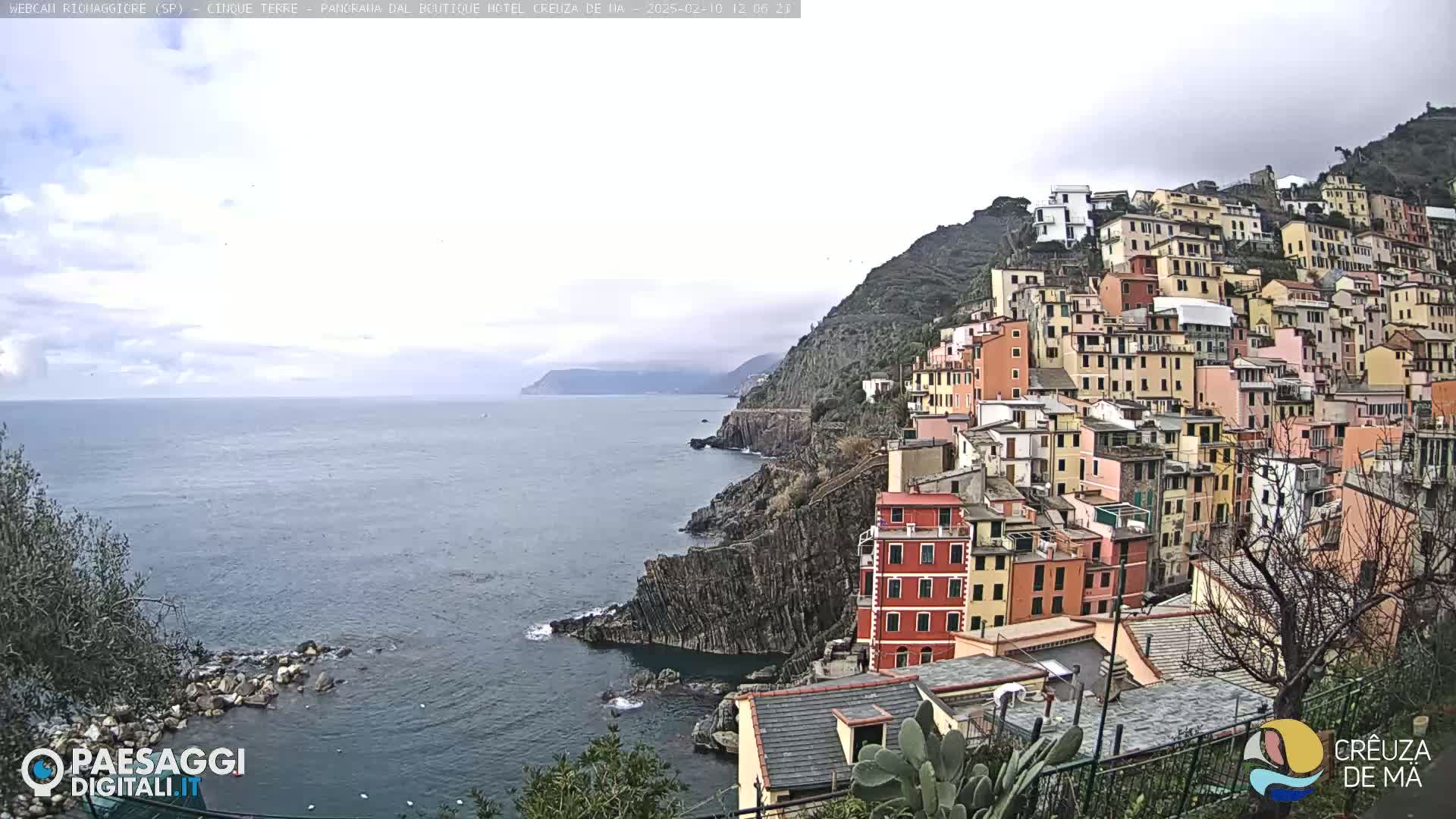 A coastal town with colorful buildings on a hillside overlooking a calm sea under an overcast sky.