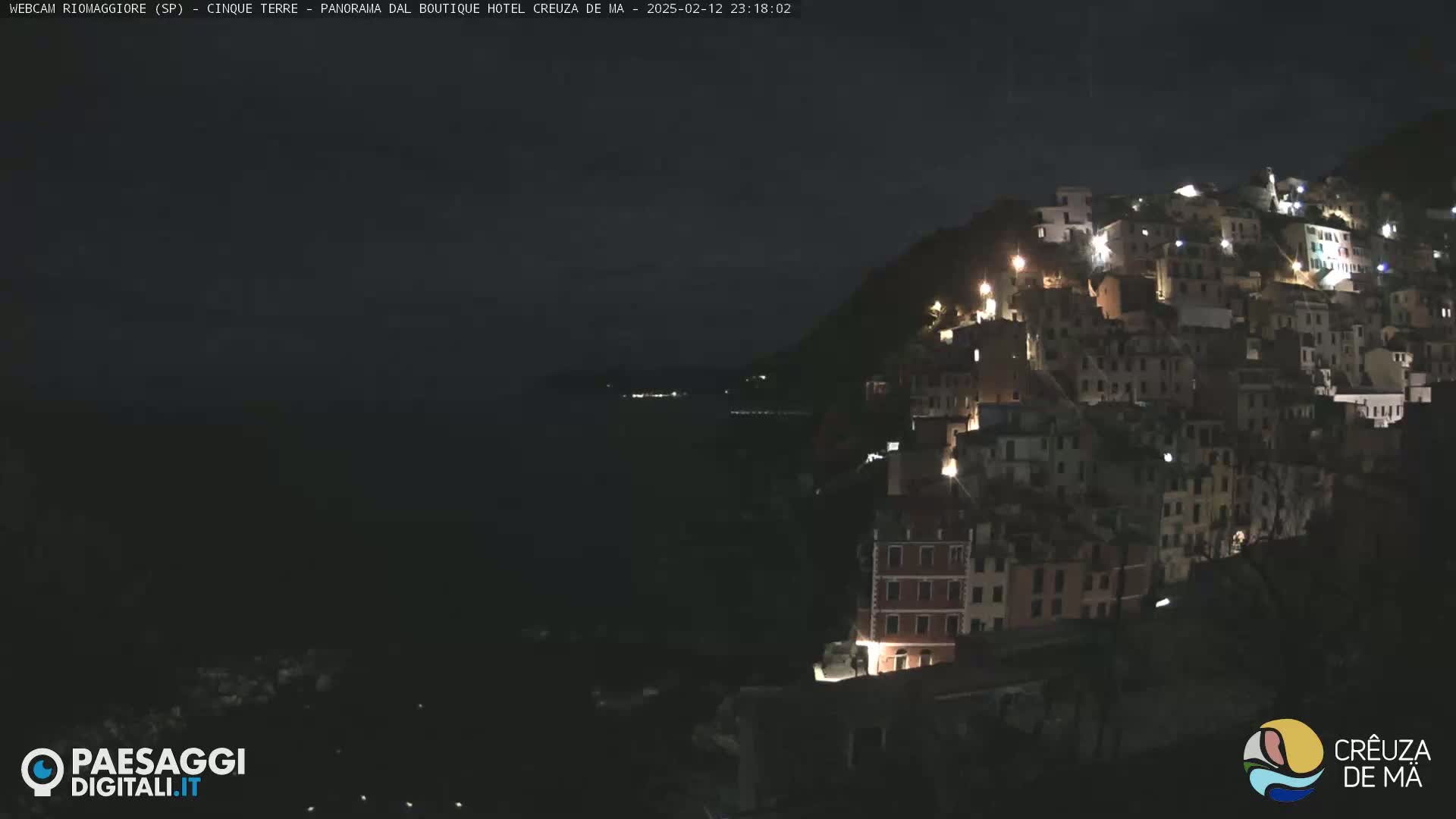 A nighttime, coastal village clings to a hillside overlooking a dark body of water.