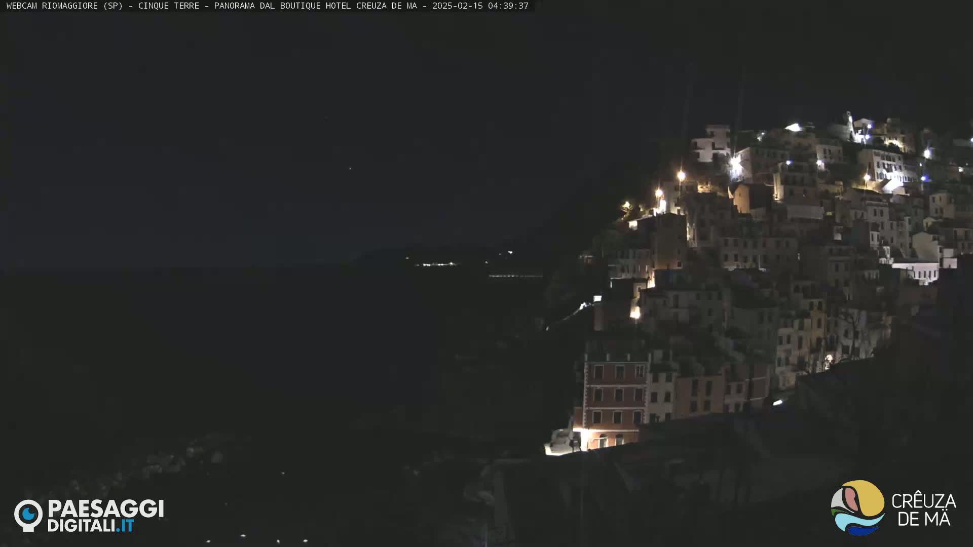 A nighttime, seaside village is illuminated with scattered lights against a dark sky.