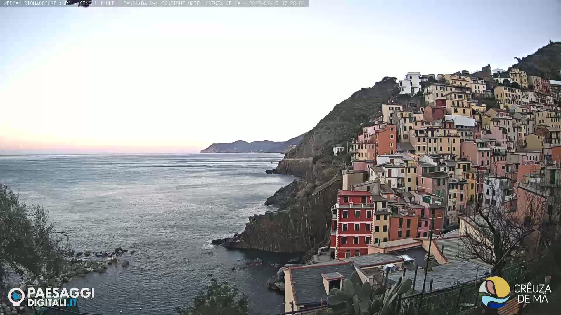 A colorful hillside village overlooks a calm sea under a clear, light-blue sky.