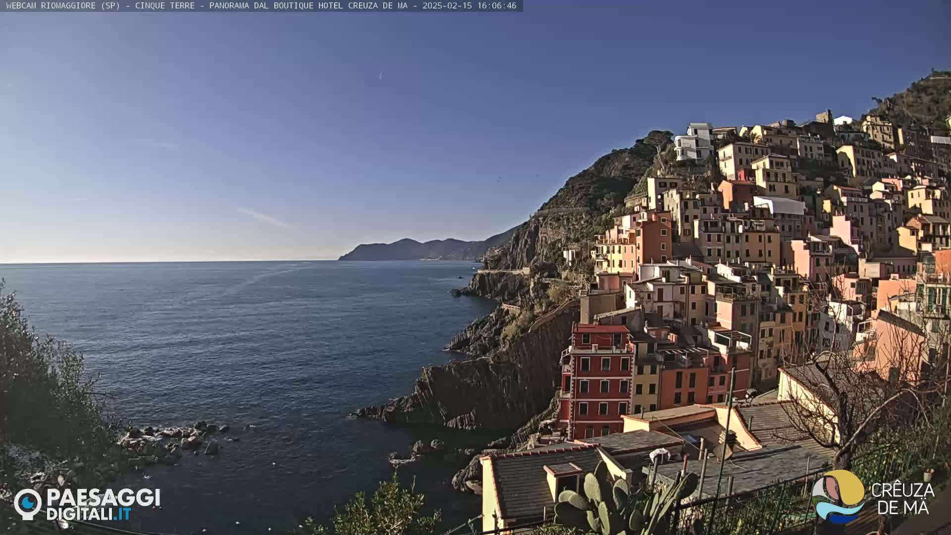 A colorful hillside town overlooks a calm blue sea under a clear blue sky.