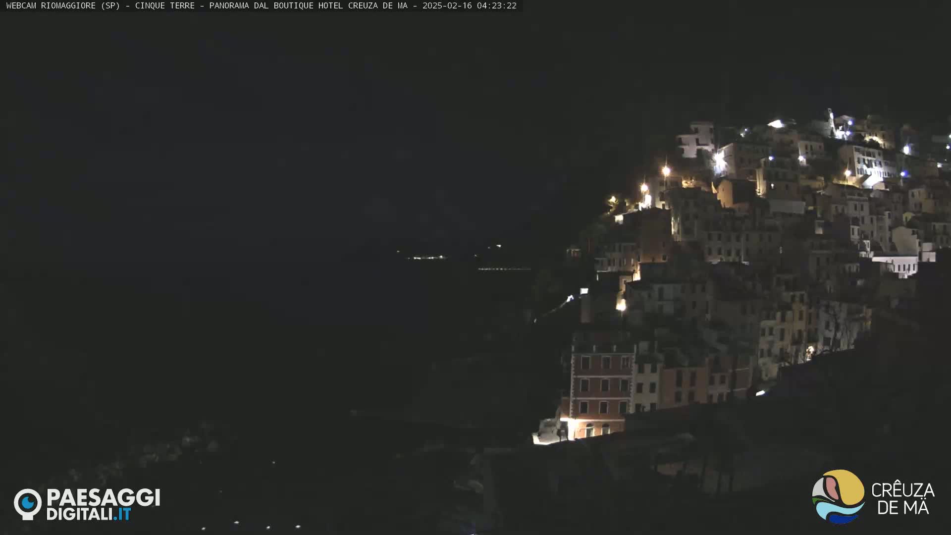A hillside village with illuminated buildings is visible at night, overlooking a dark body of water.