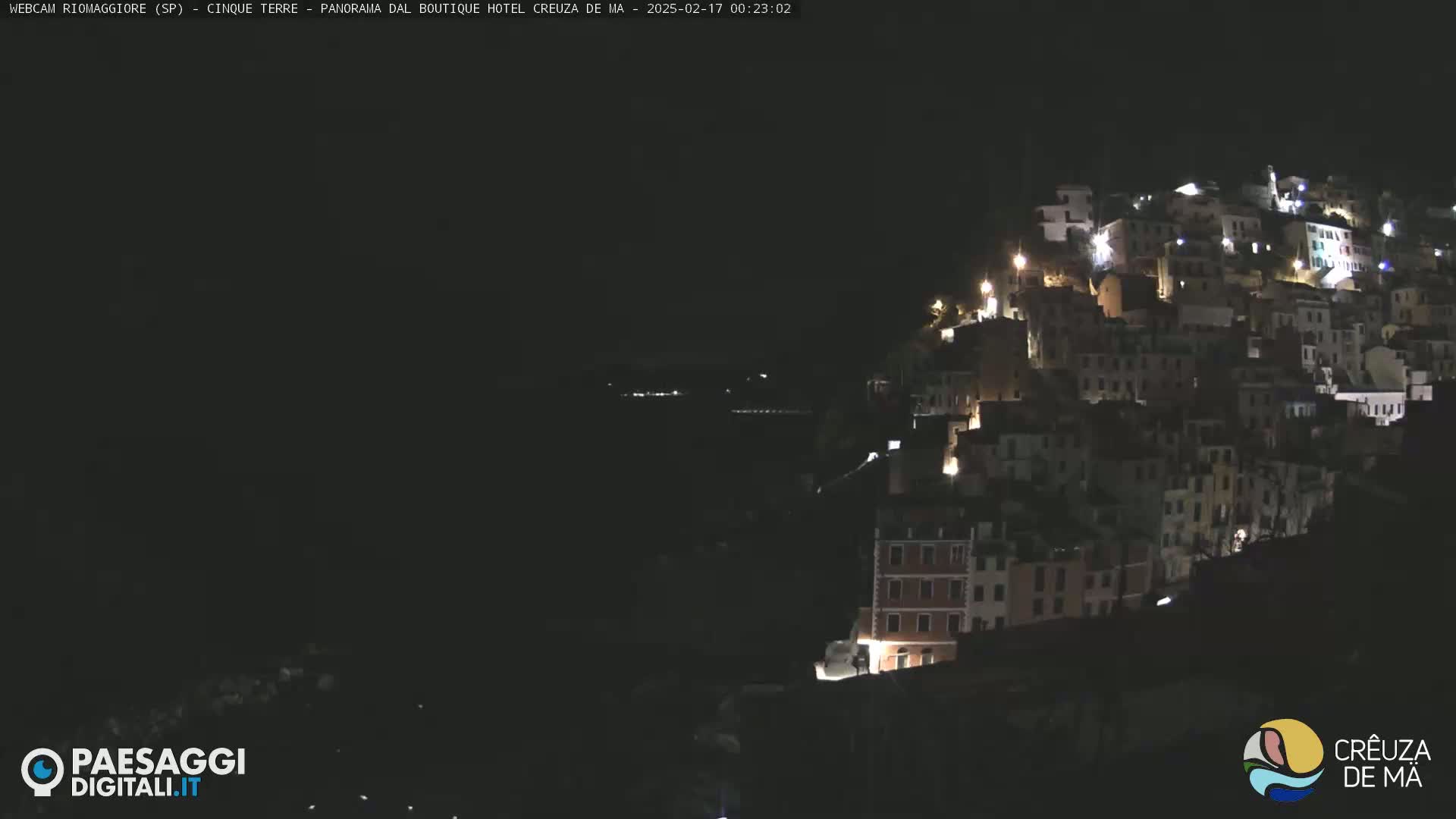 A hillside village is illuminated at night, with the lights of buildings visible against a dark, clear sky.