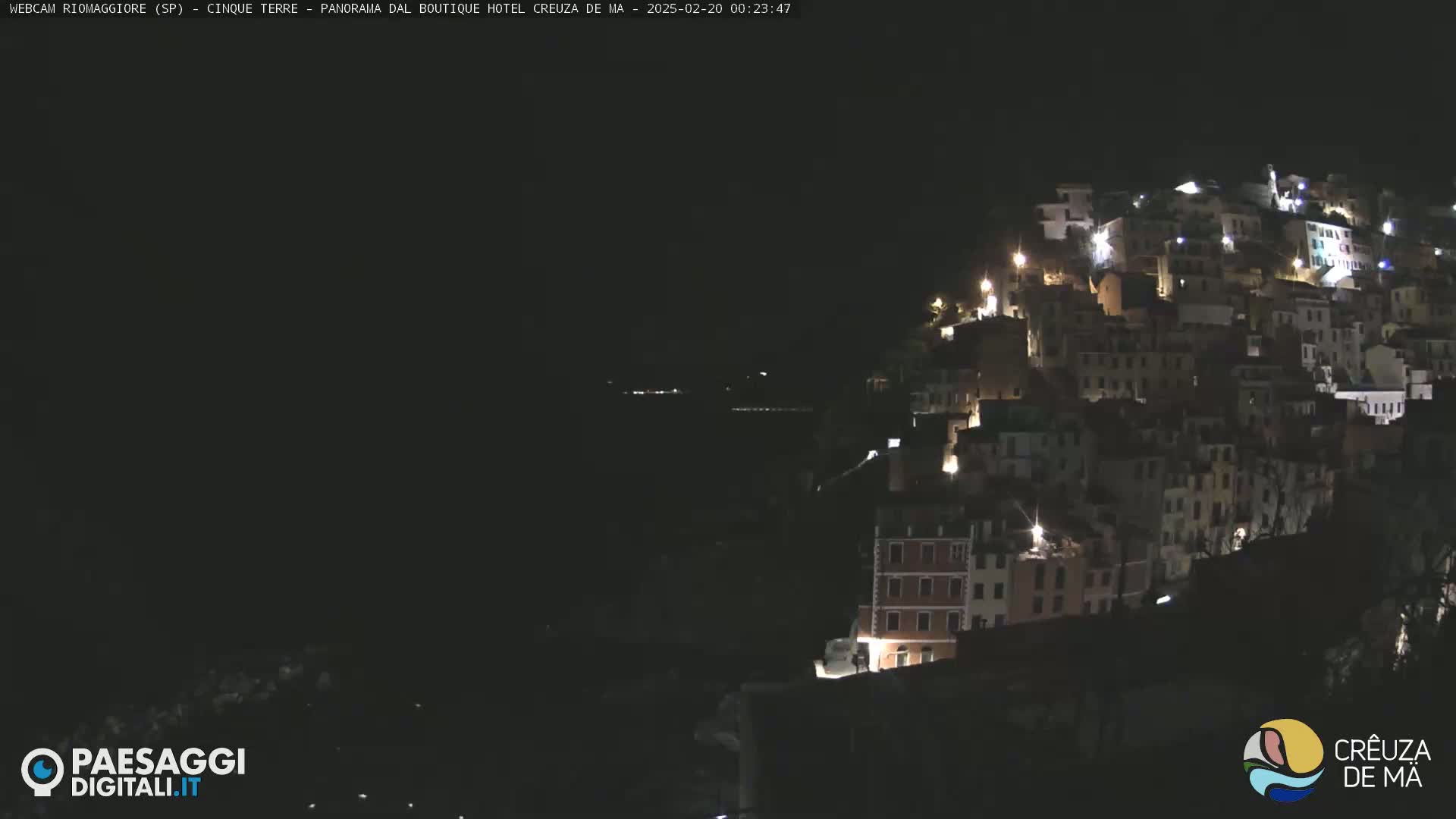 A hillside village is illuminated at night, overlooking a dark body of water.