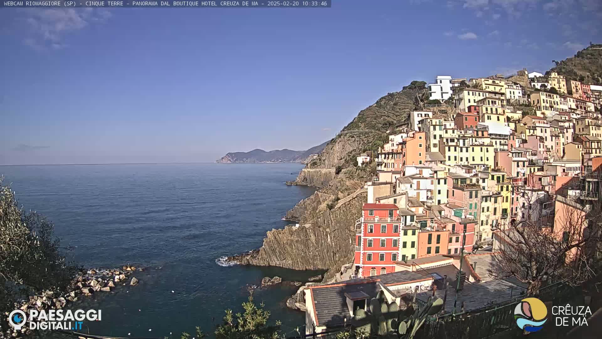 A picturesque coastal town with colorful buildings clinging to a steep hillside overlooks a calm, blue sea under a clear sky.