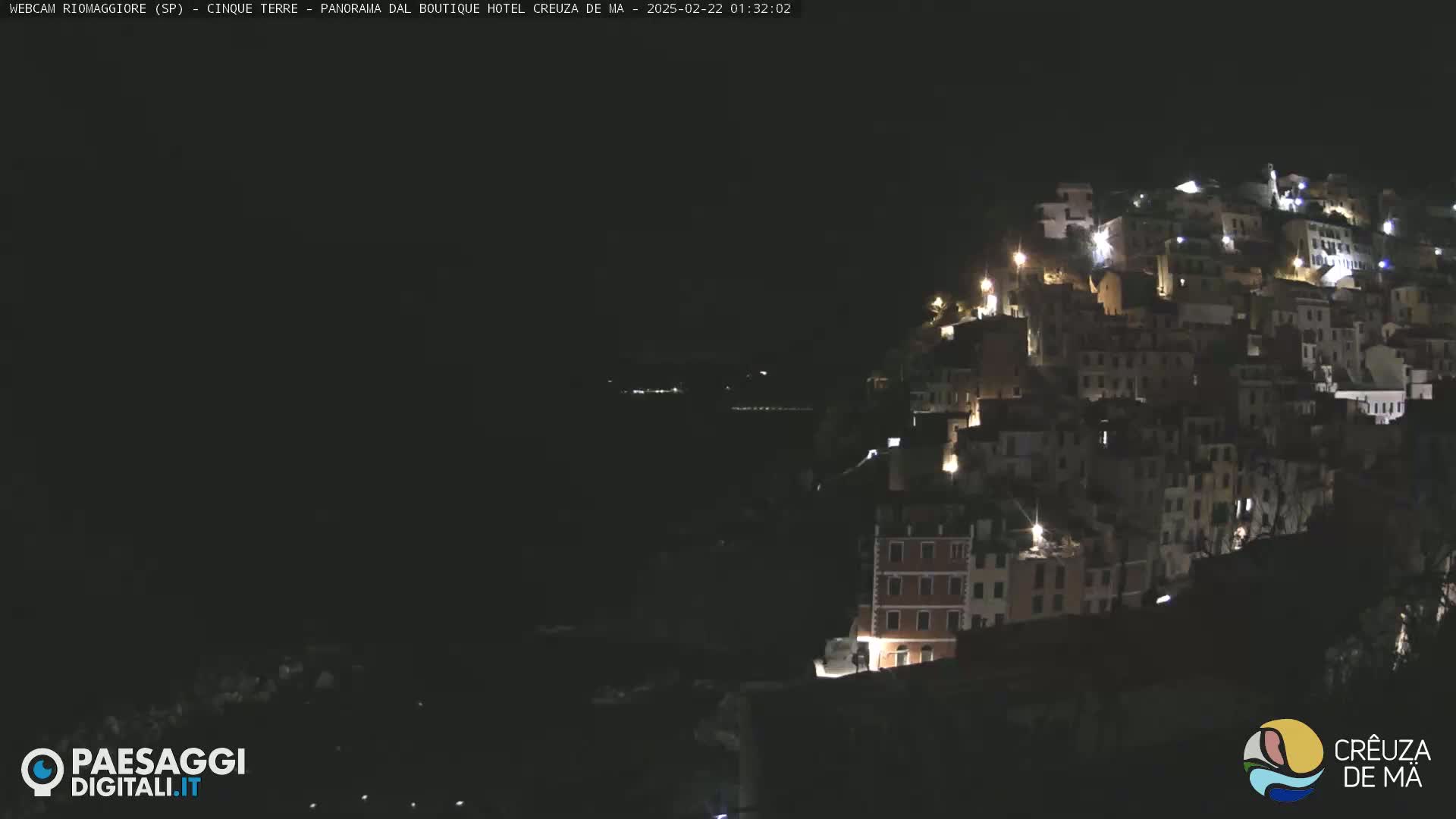 A nighttime, coastal town is illuminated by scattered lights on a dark hillside.