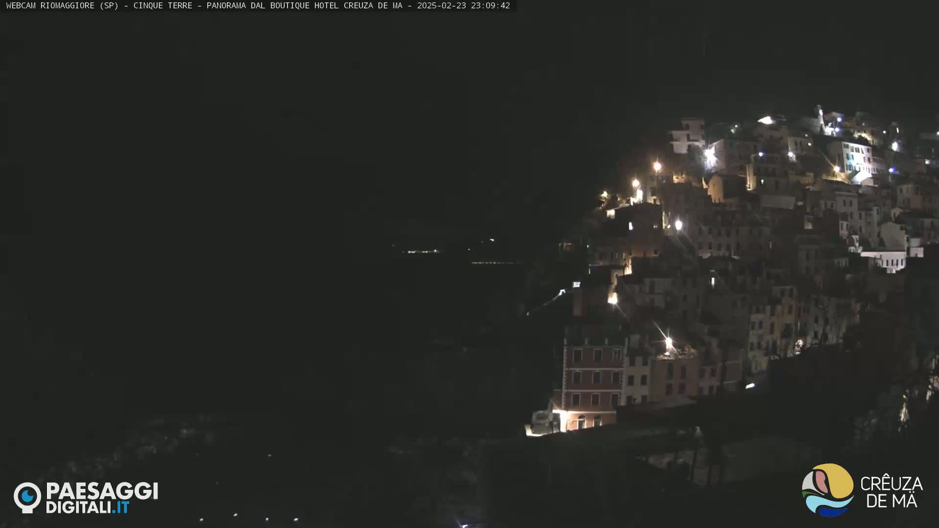 A nighttime, long shot of a hillside village with illuminated buildings.