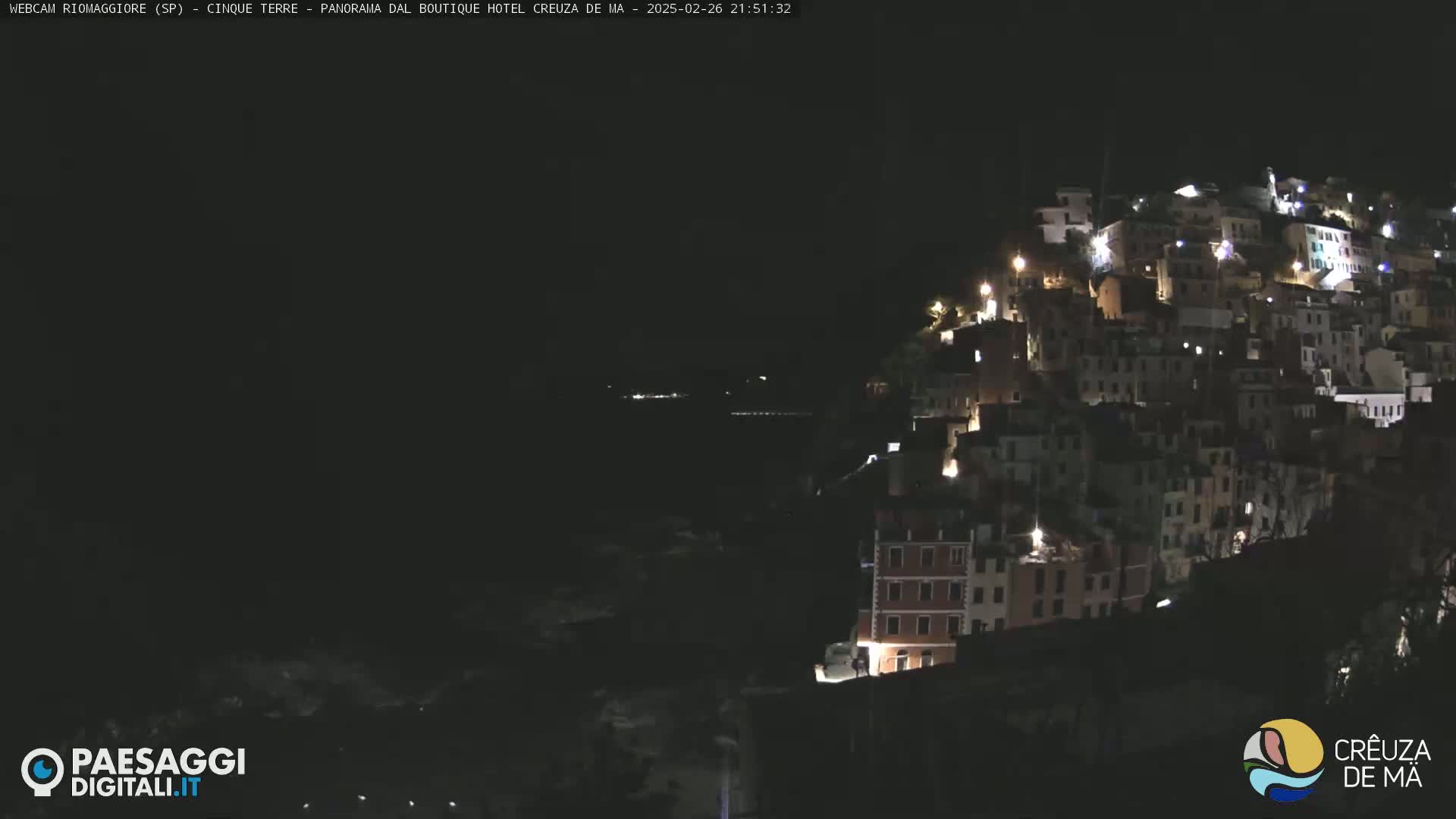 A nighttime view of a hillside village illuminated by lights, overlooking a dark body of water.