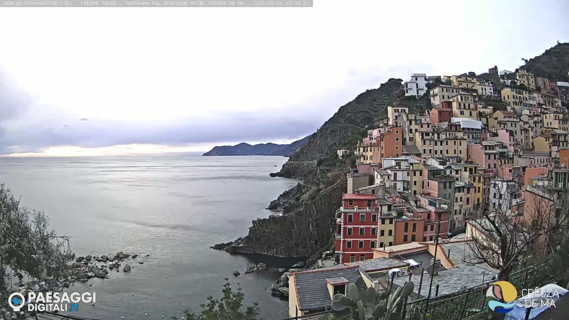 A colorful hillside village overlooks a calm sea under an overcast sky.