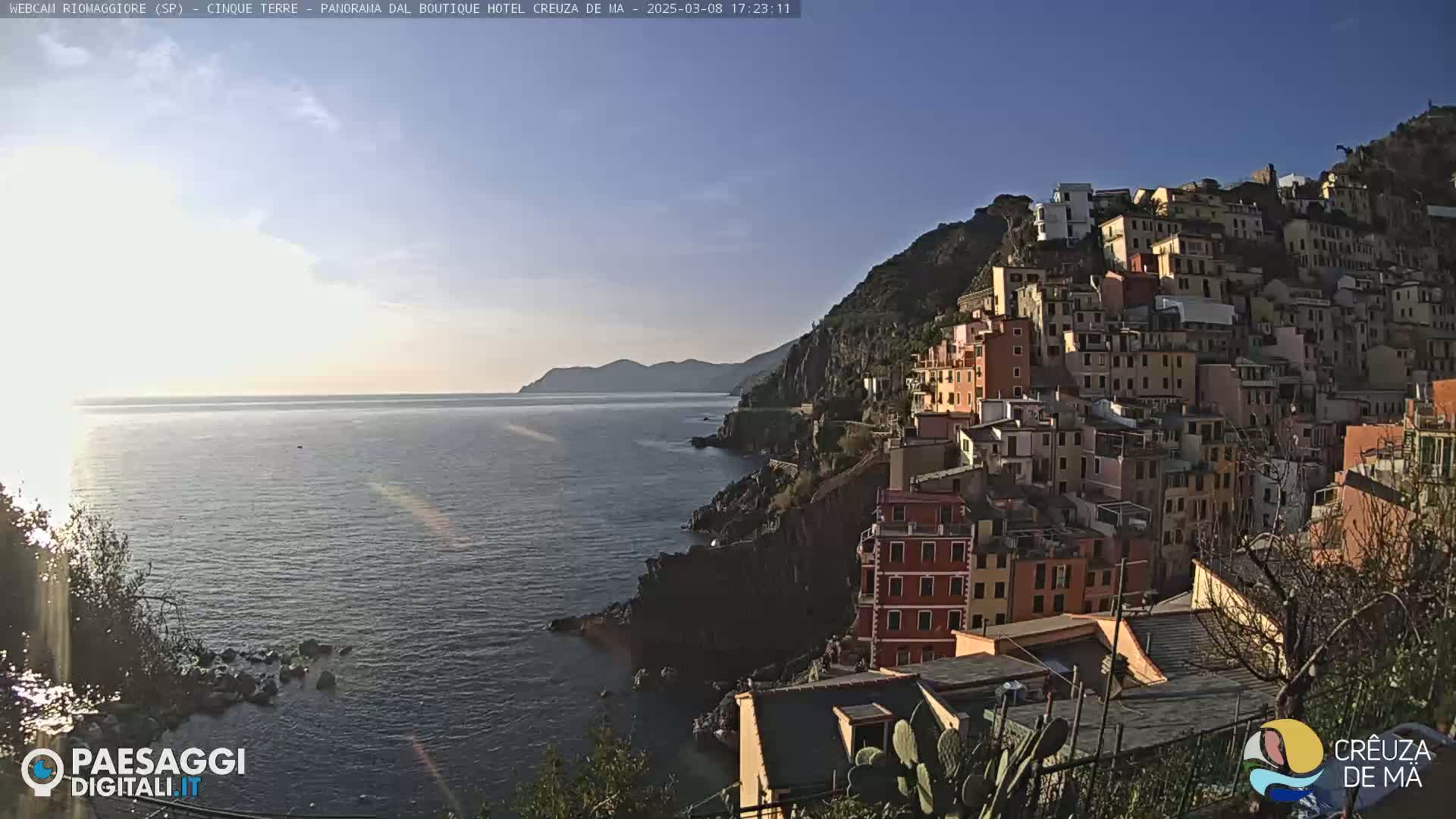 A colorful hillside village overlooks a calm sea under a clear, bright sky.