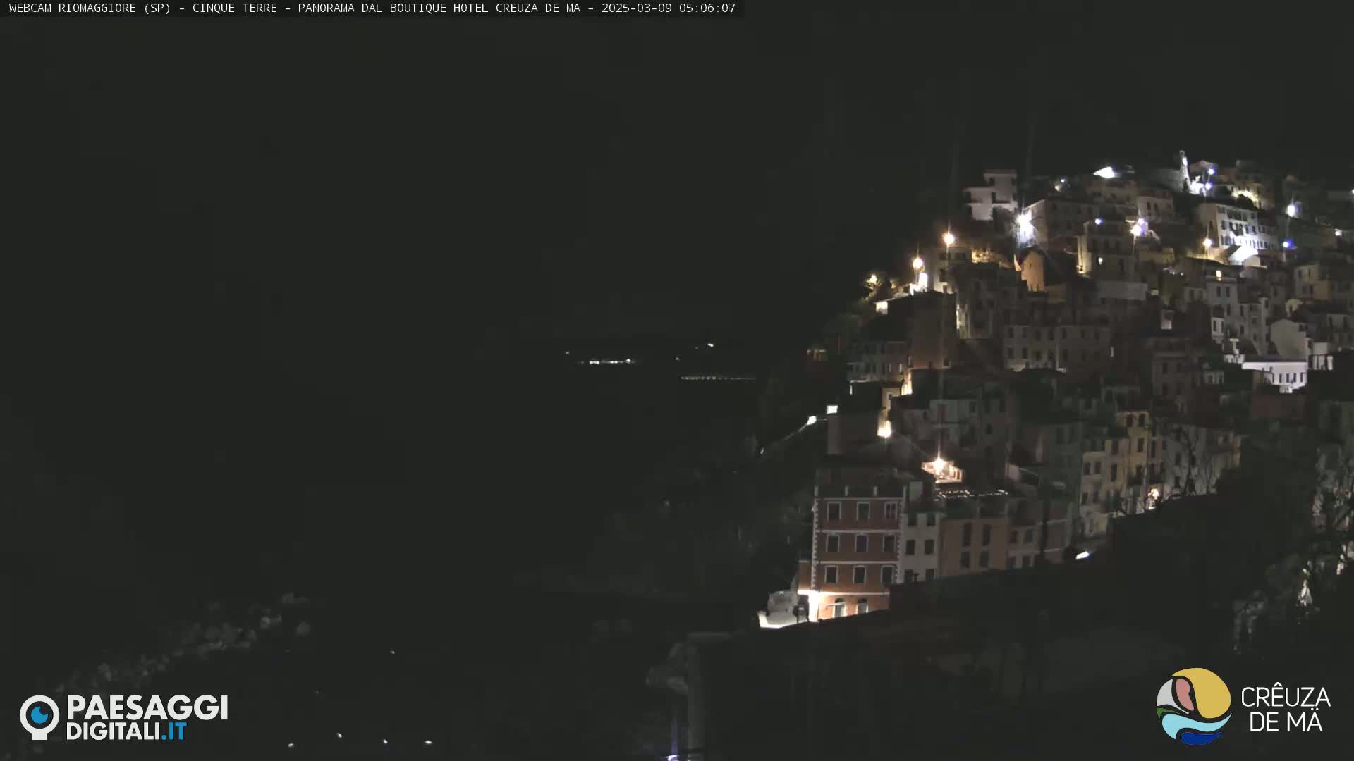 A hillside town is illuminated at night, overlooking a dark body of water.