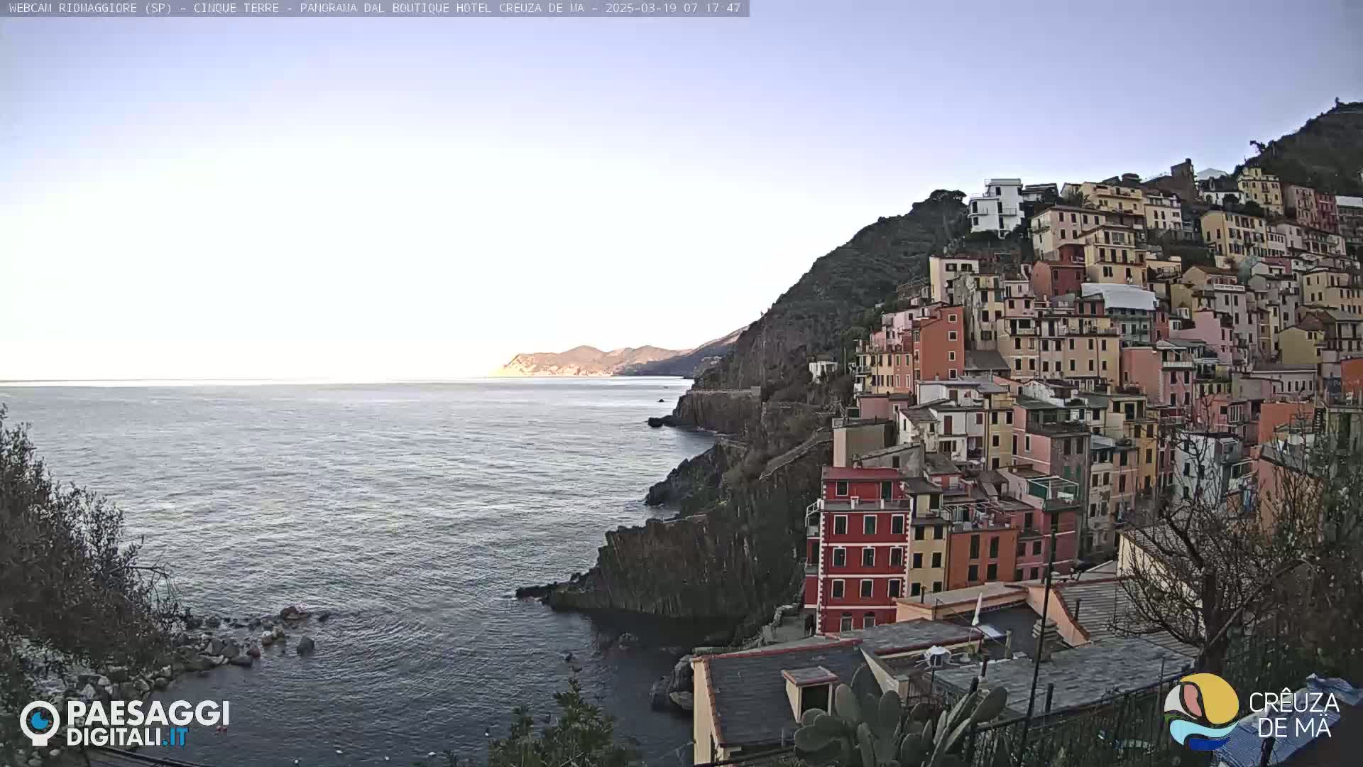 A coastal town with colorful buildings stacked on a hillside overlooking a calm sea under a clear sky.