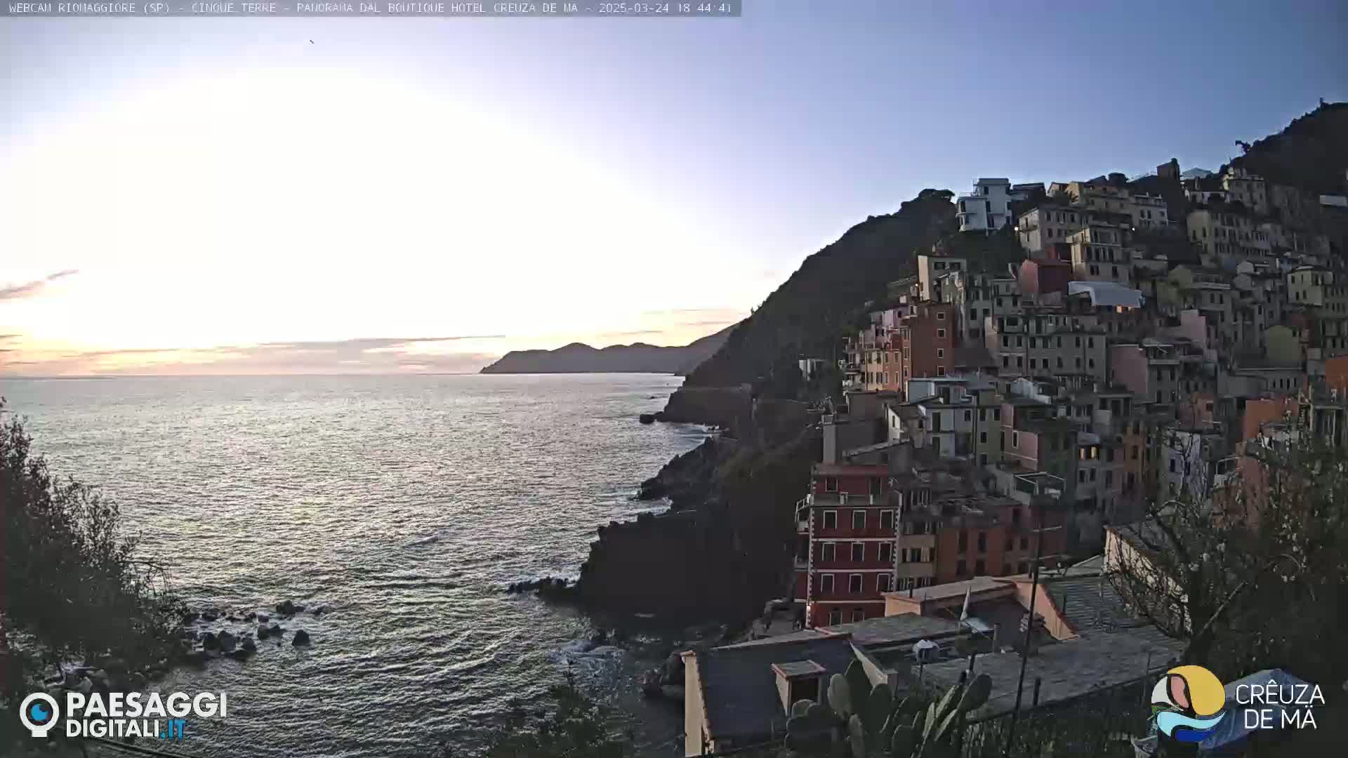 A coastal town nestled on a hillside overlooking a calm sea at sunset.