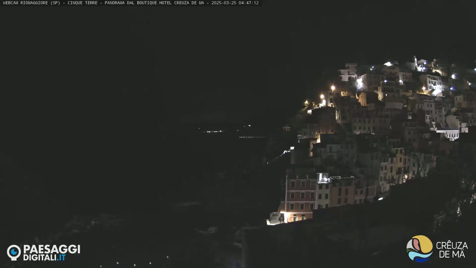 A nighttime view of a hillside town with many illuminated buildings overlooking a dark body of water.