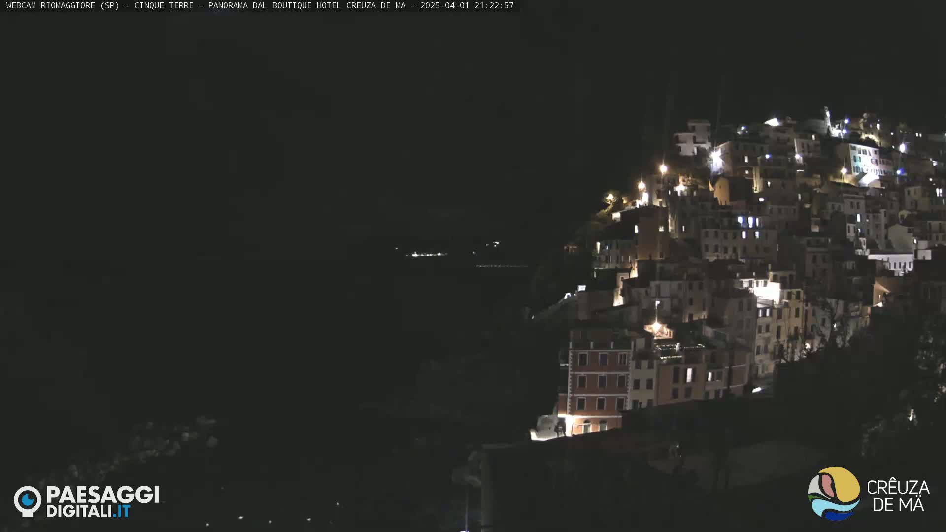 A hillside town is brightly lit at night, overlooking a dark body of water.