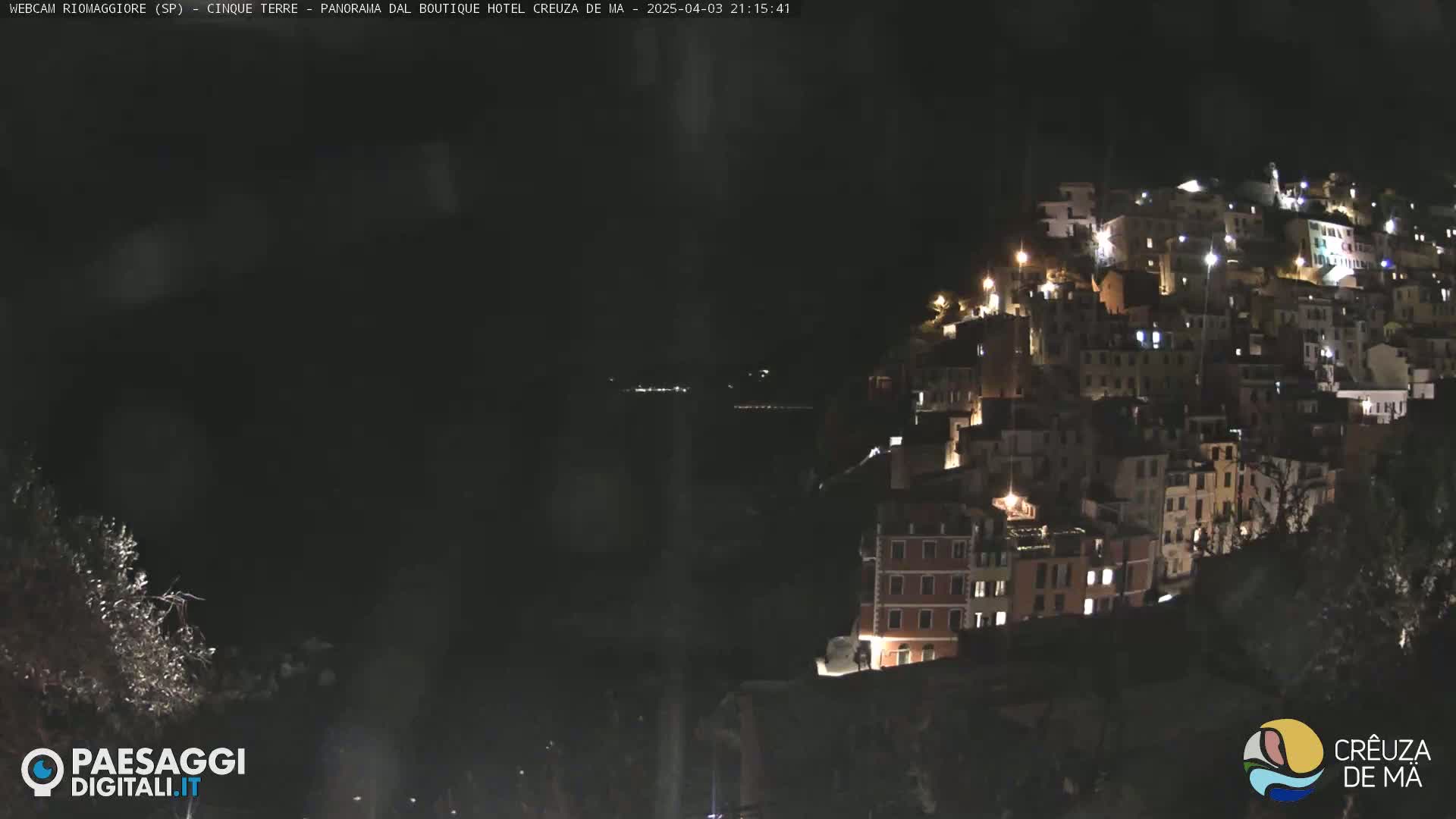A hillside town is illuminated at night, overlooking a dark body of water under a clear, dark sky.