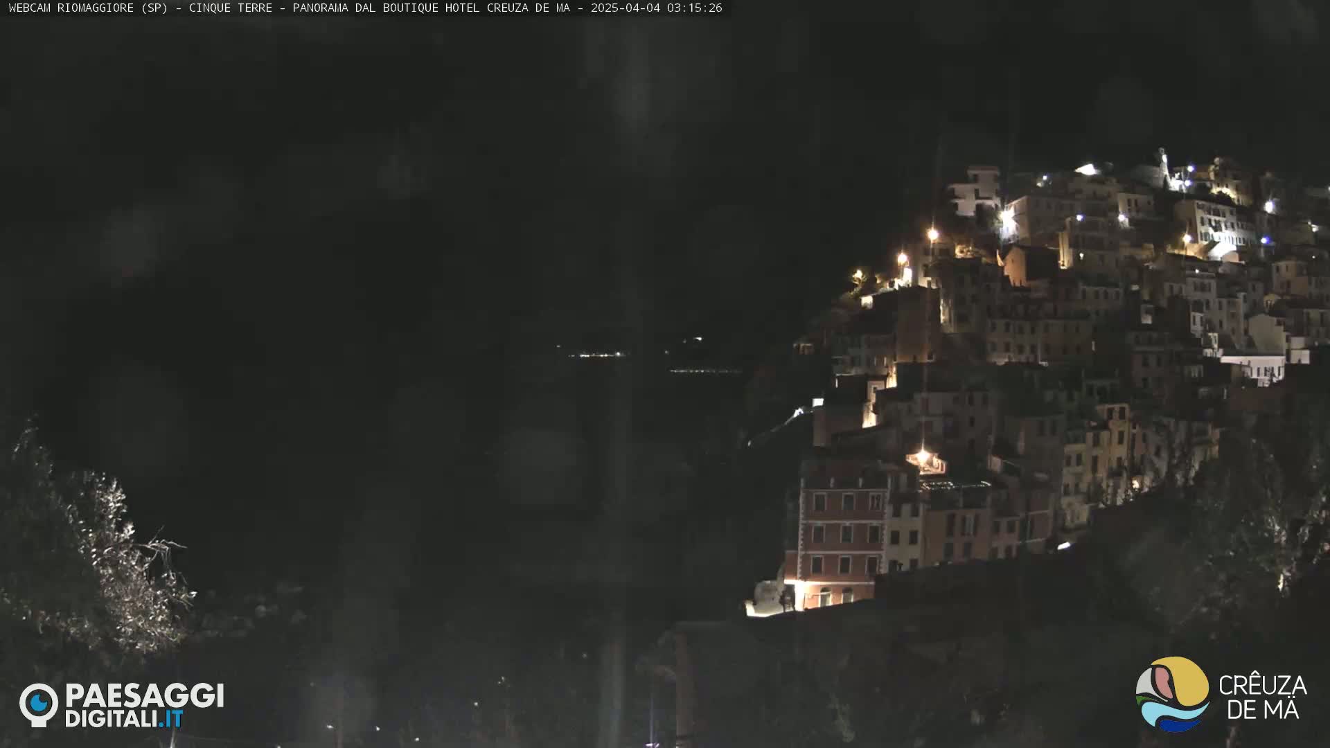 A hillside town is illuminated at night, overlooking a dark body of water.