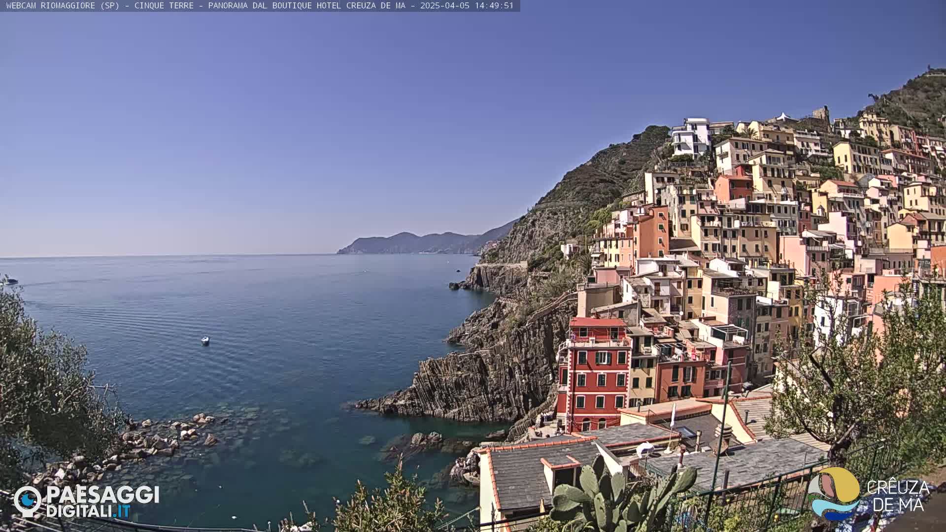 A colorful village clings to a steep hillside overlooking a calm blue sea under a clear sky.