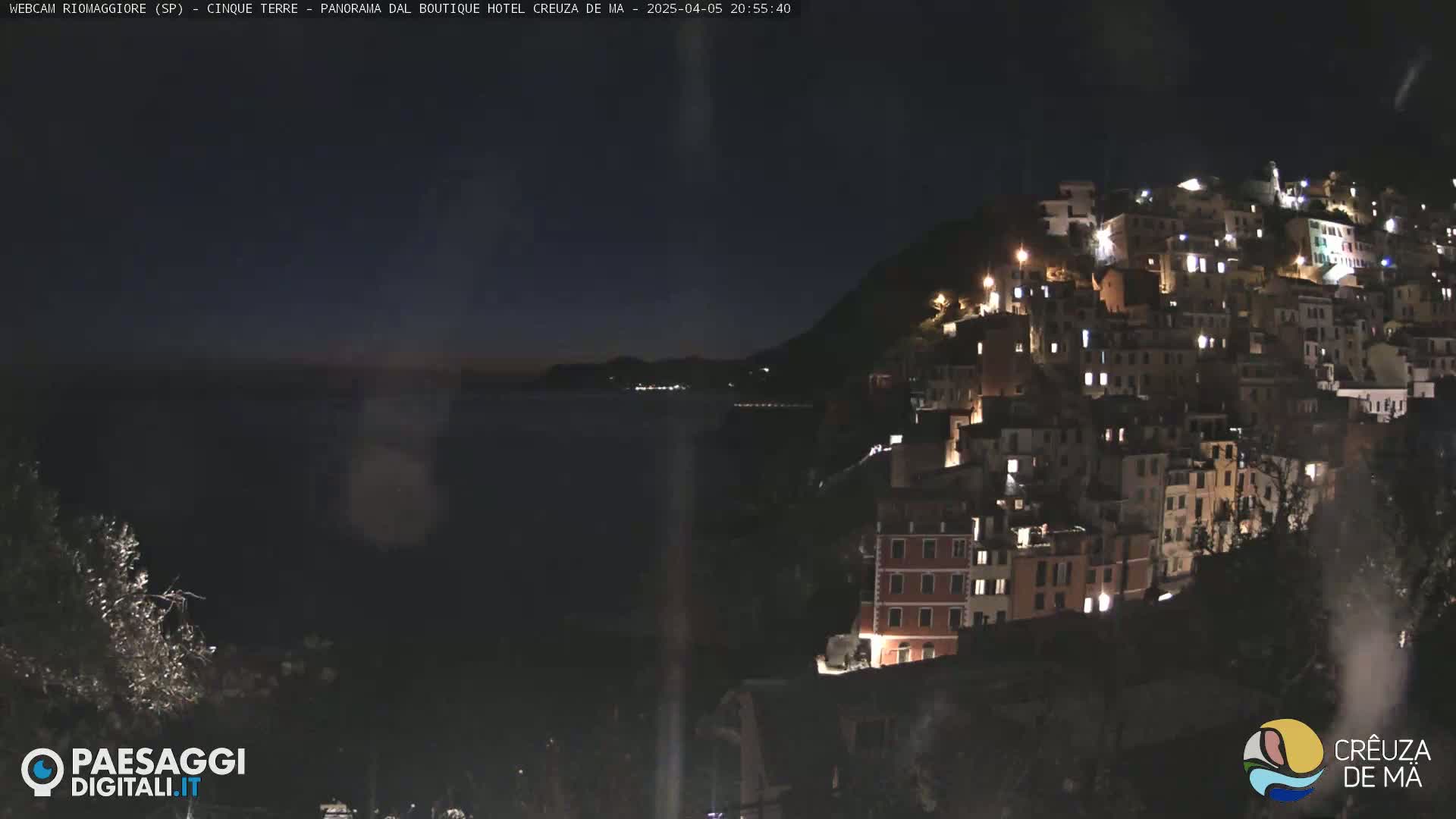 A nighttime view of a hillside town with numerous illuminated buildings overlooking a dark body of water under a clear sky.