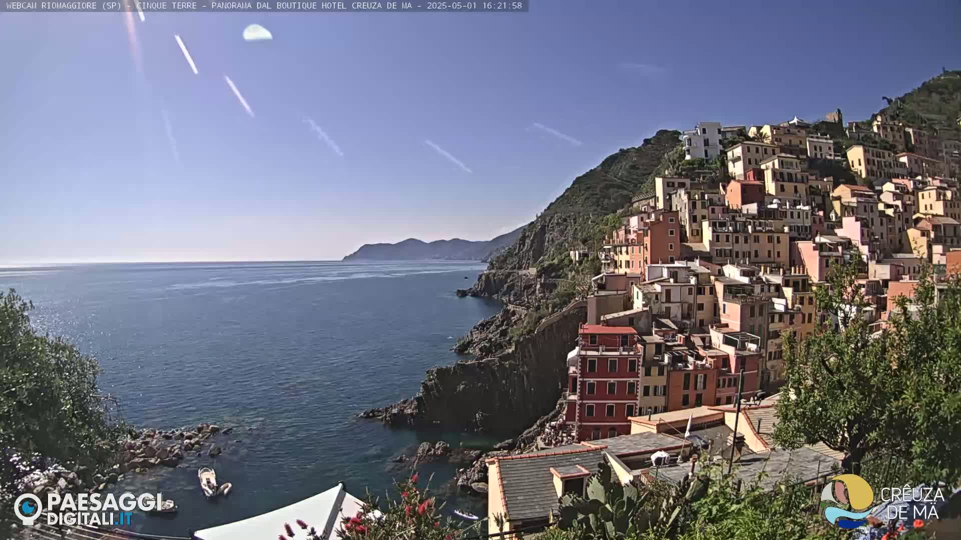 A colorful village clings to a steep hillside overlooking a calm sea under a clear blue sky.