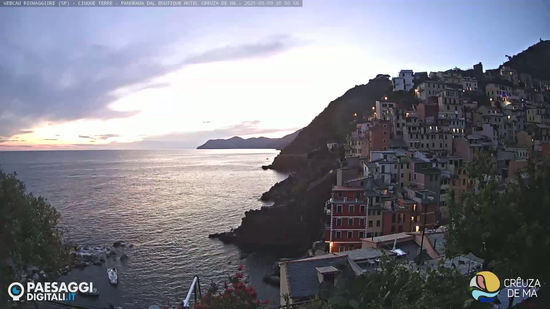 A picturesque coastal town clings to a cliffside overlooking a calm sea at sunset.