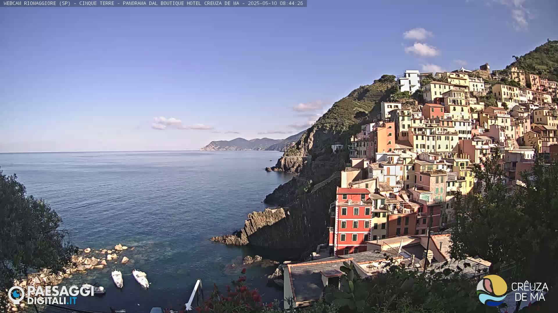 A picturesque coastal village clings to a hillside overlooking a calm sea under a clear blue sky.