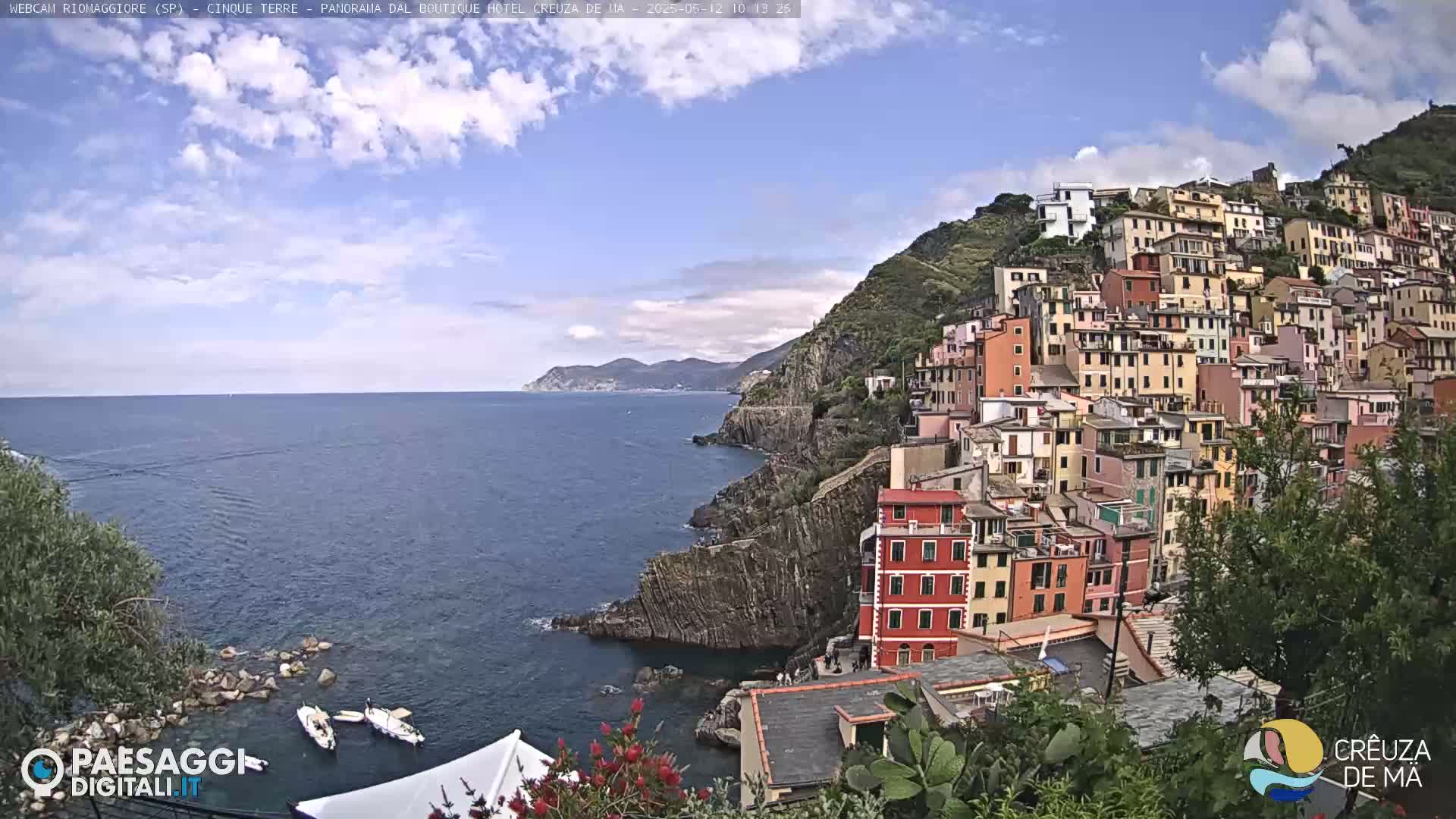 A picturesque coastal town with colorful buildings clinging to a hillside overlooking a calm sea under a partly cloudy sky.