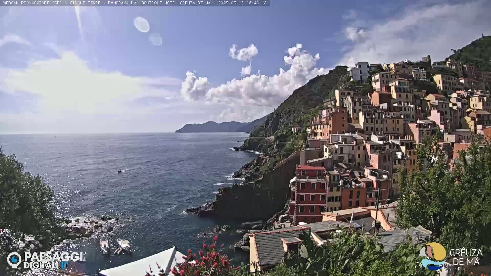 A coastal village of colorful buildings clings to a hillside overlooking a calm sea under a partly cloudy sky.