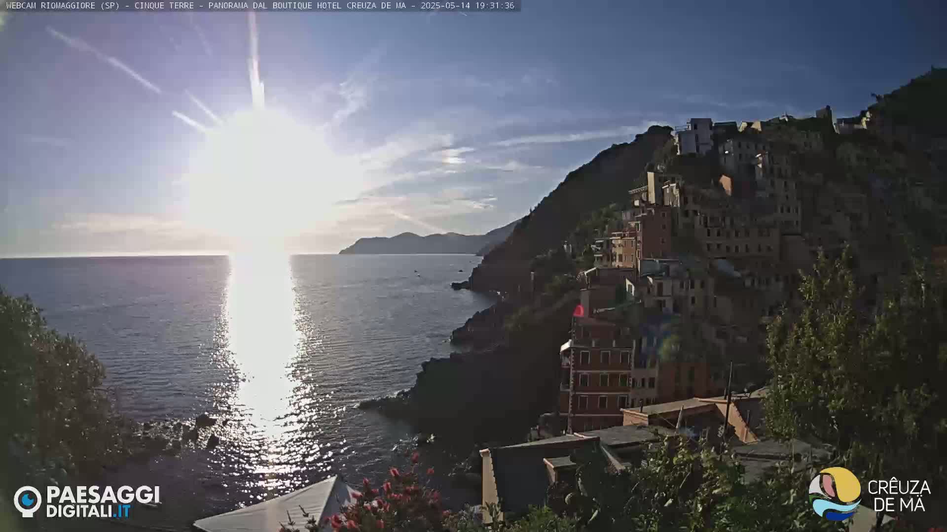 A bright, sunny day overlooks a village of colorful buildings clinging to a steep hillside overlooking a calm sea.