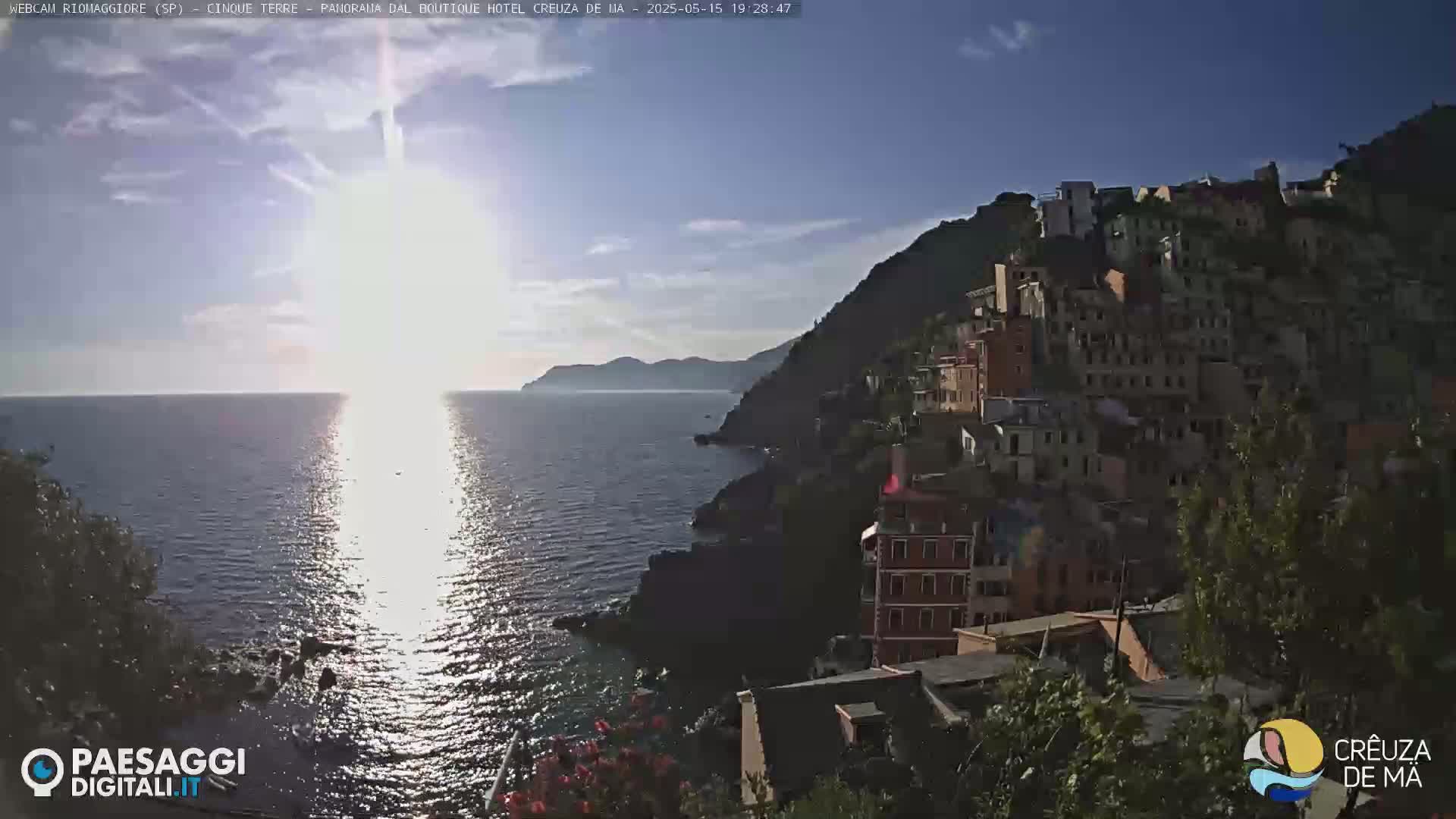 A coastal town built into a hillside overlooks a calm sea reflecting the bright sun on a clear day.