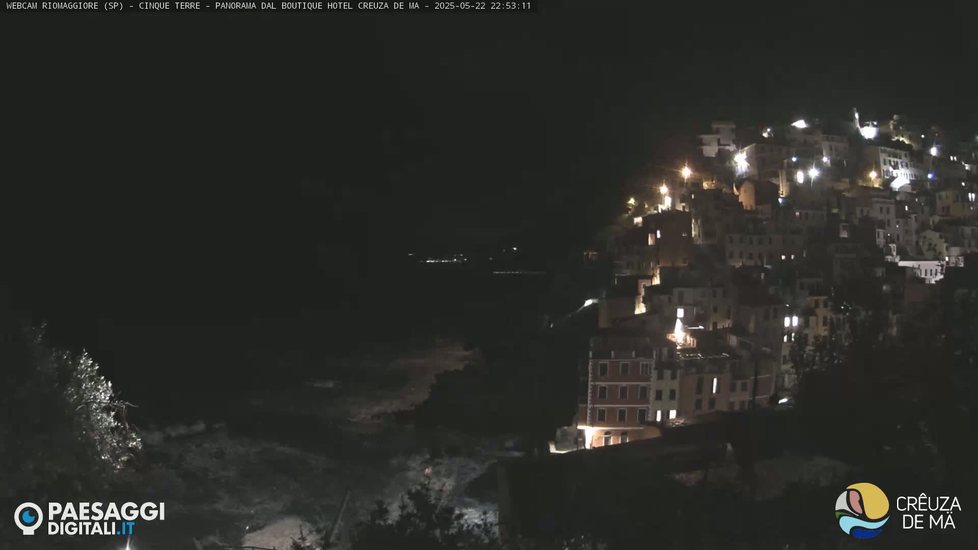 A nighttime view of a coastal town illuminated by lights, with dark water visible below.