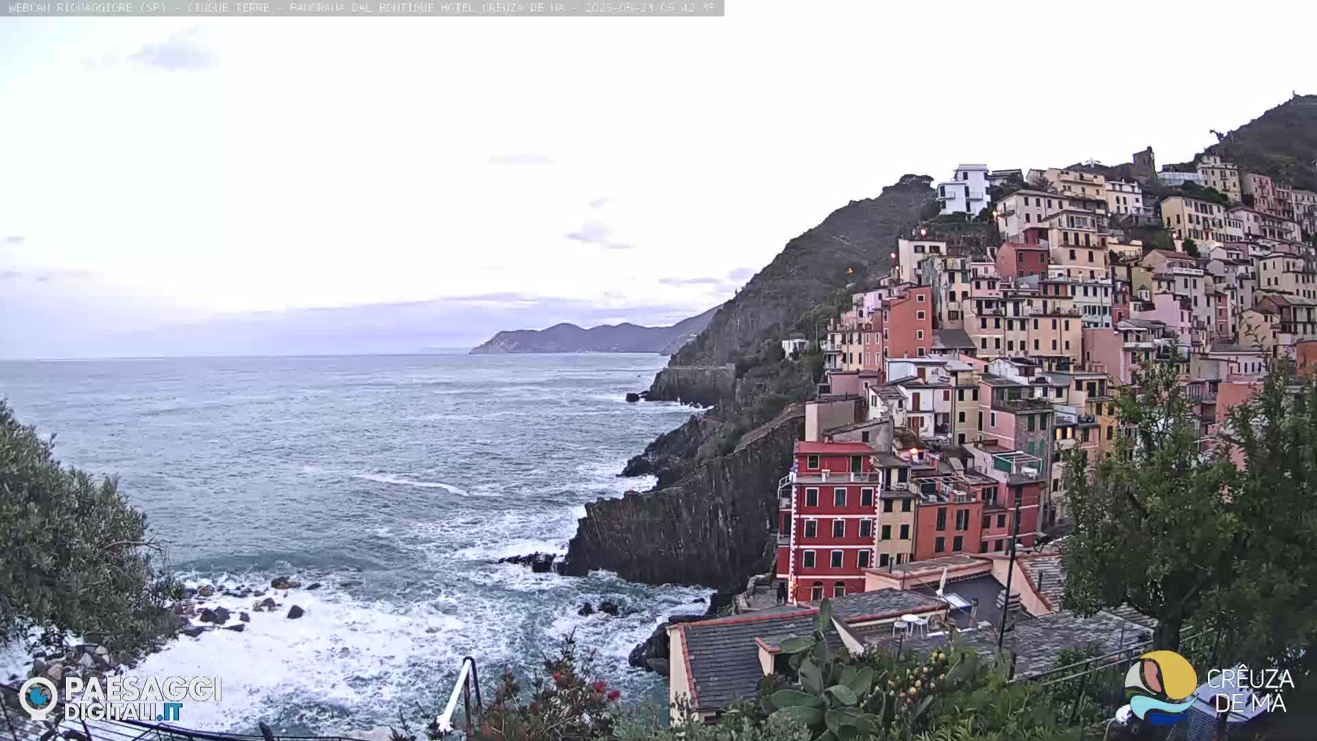 A colorful hillside town overlooks a choppy sea under an overcast sky.