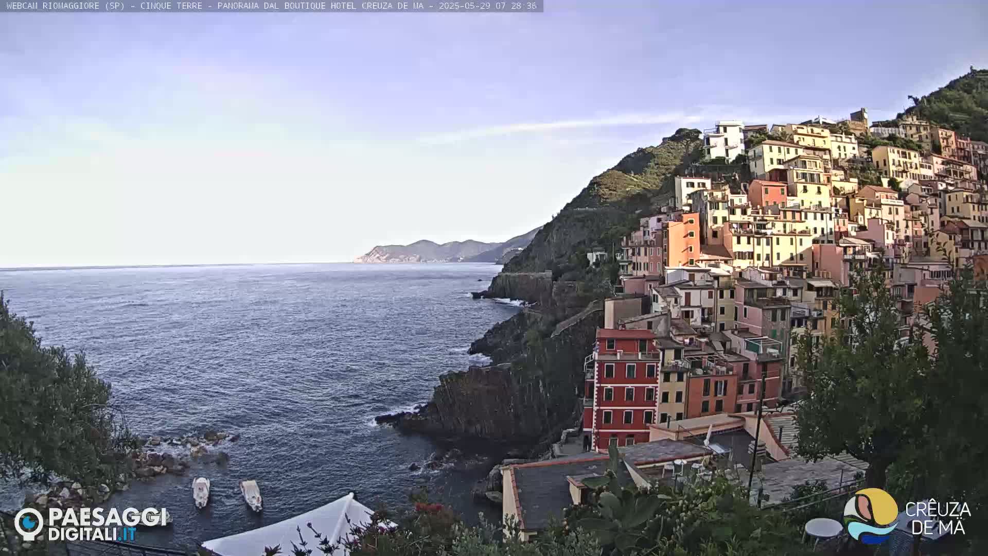 A picturesque coastal town with colorful buildings clings to a steep hillside overlooking a calm sea under a clear sky.