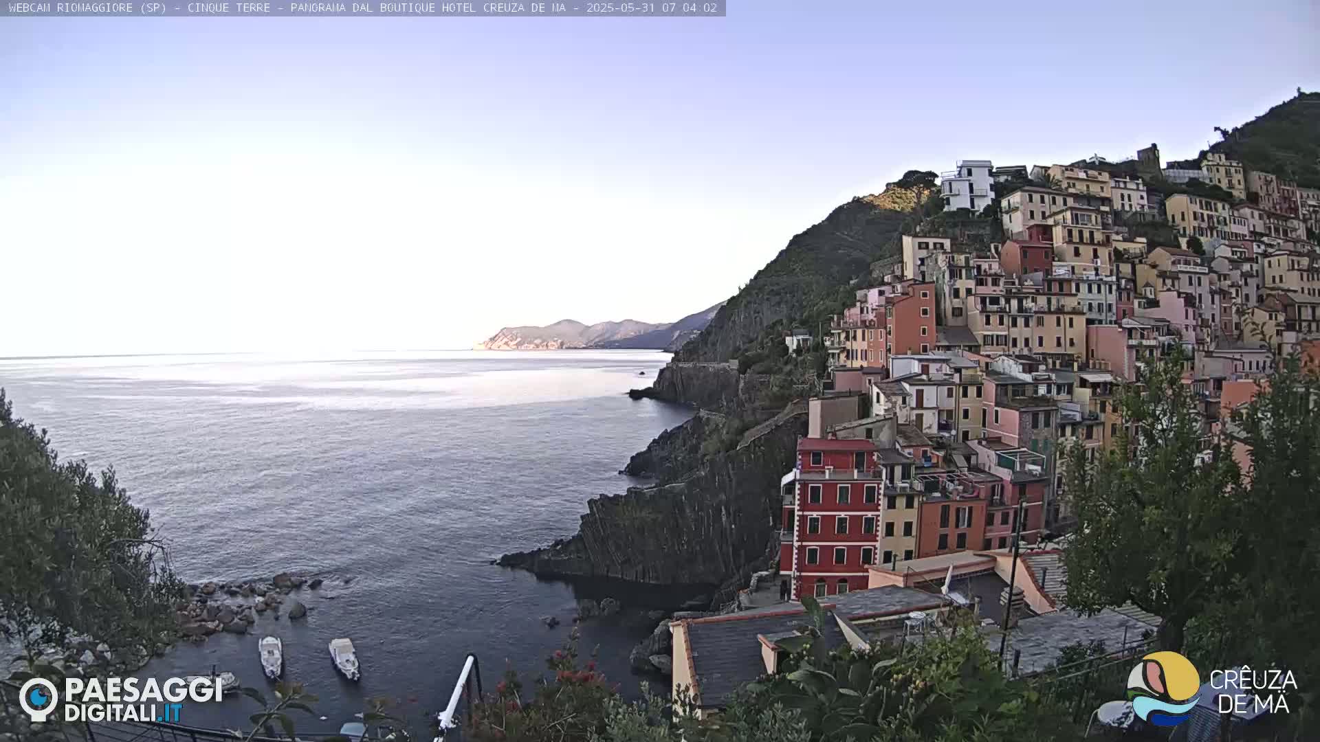 A coastal village of colorful buildings clings to a steep hillside overlooking a calm sea under a clear sky.
