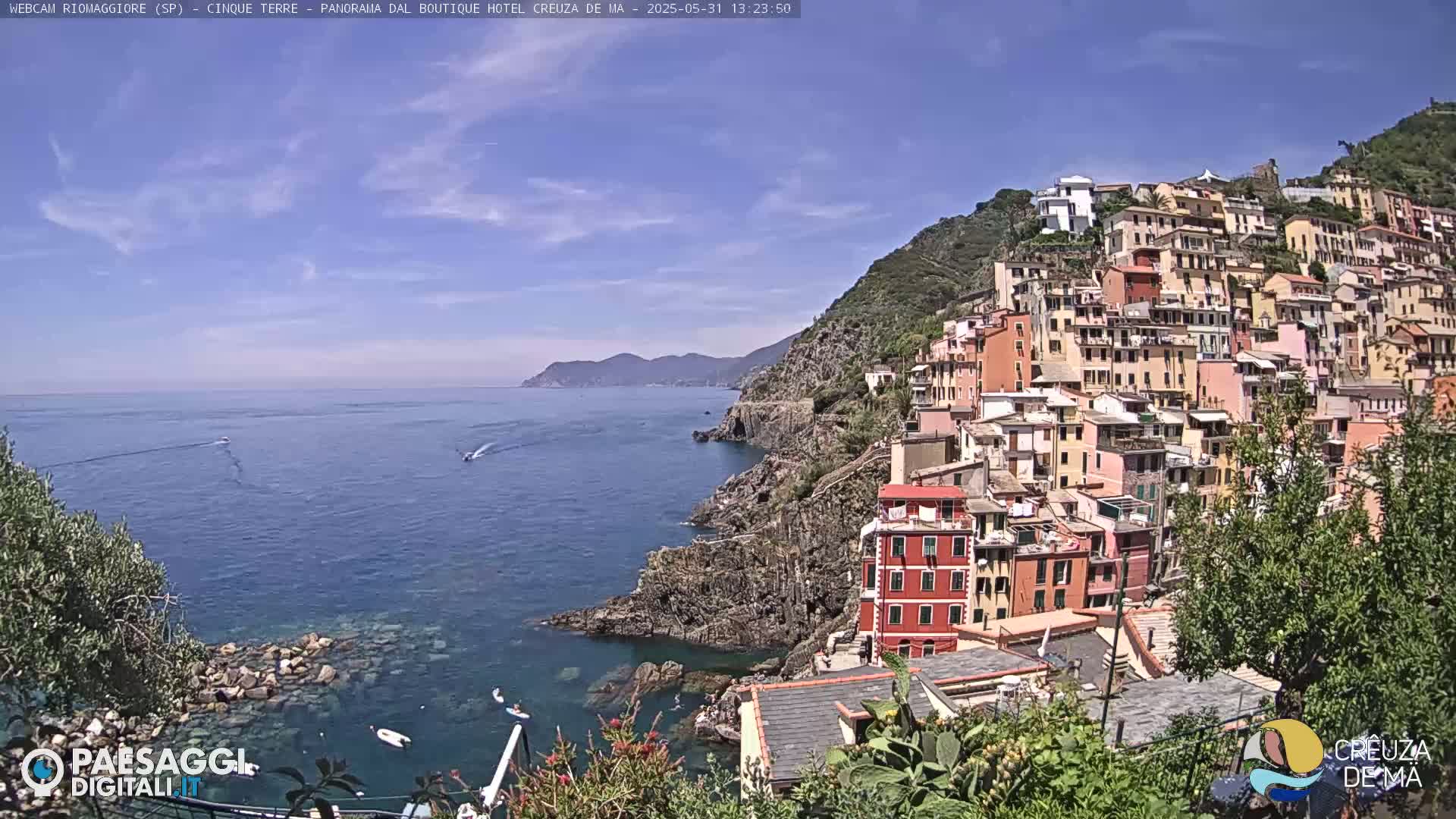 A colorful hillside village clings to a rocky coastline overlooking a calm, blue sea on a sunny day.